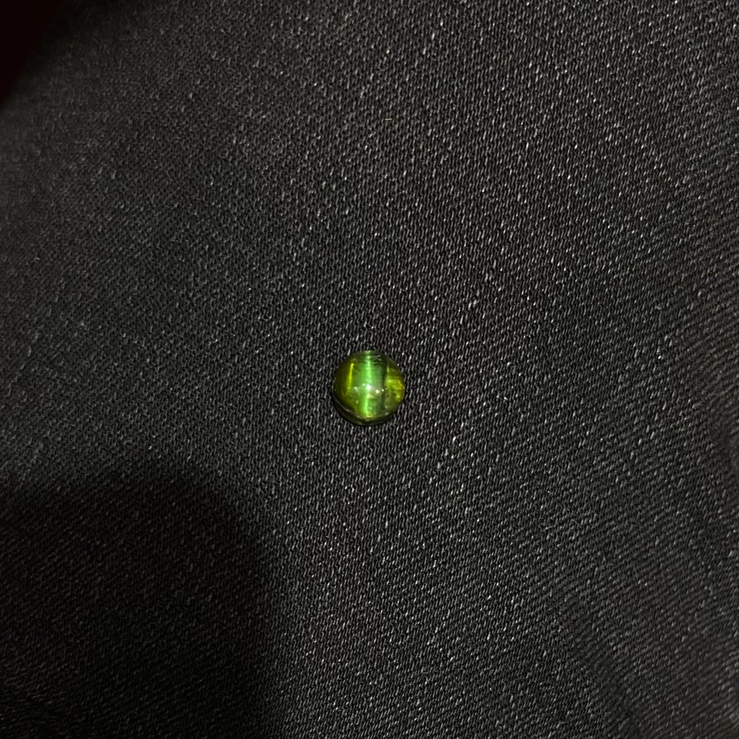 A loose, round cabochon cut green tourmaline stone that displays a cat's eye phenomenon.