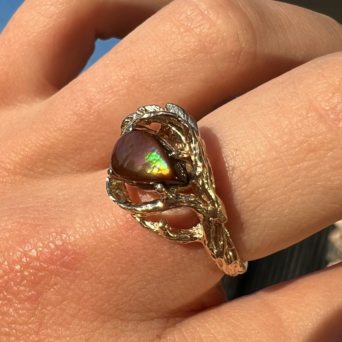 A ladies' organic style yellow gold ring set with a pear shaped cabochon cut Mexican fire agate. The stone shines green and purple.