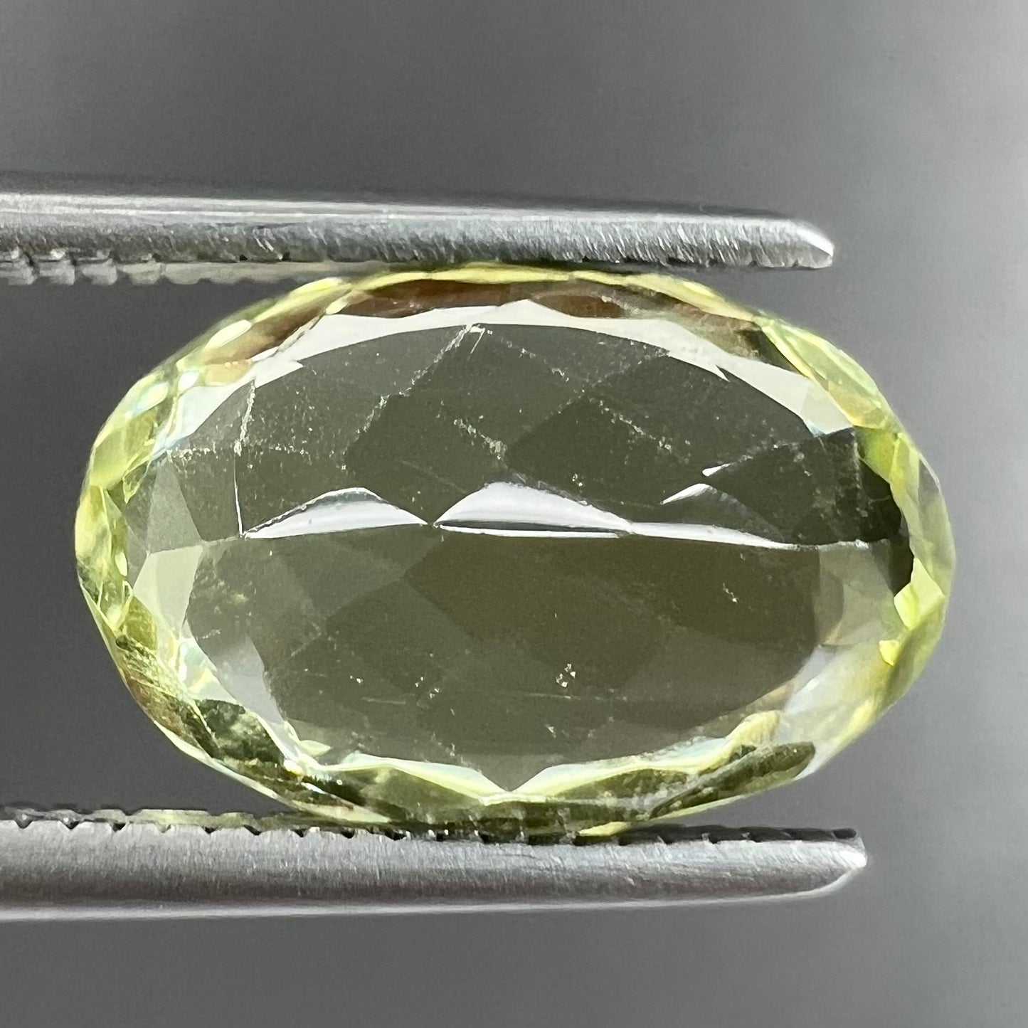 A loose, faceted oval cut chrysoberyl gemstone. The stone is a greenish yellow color.