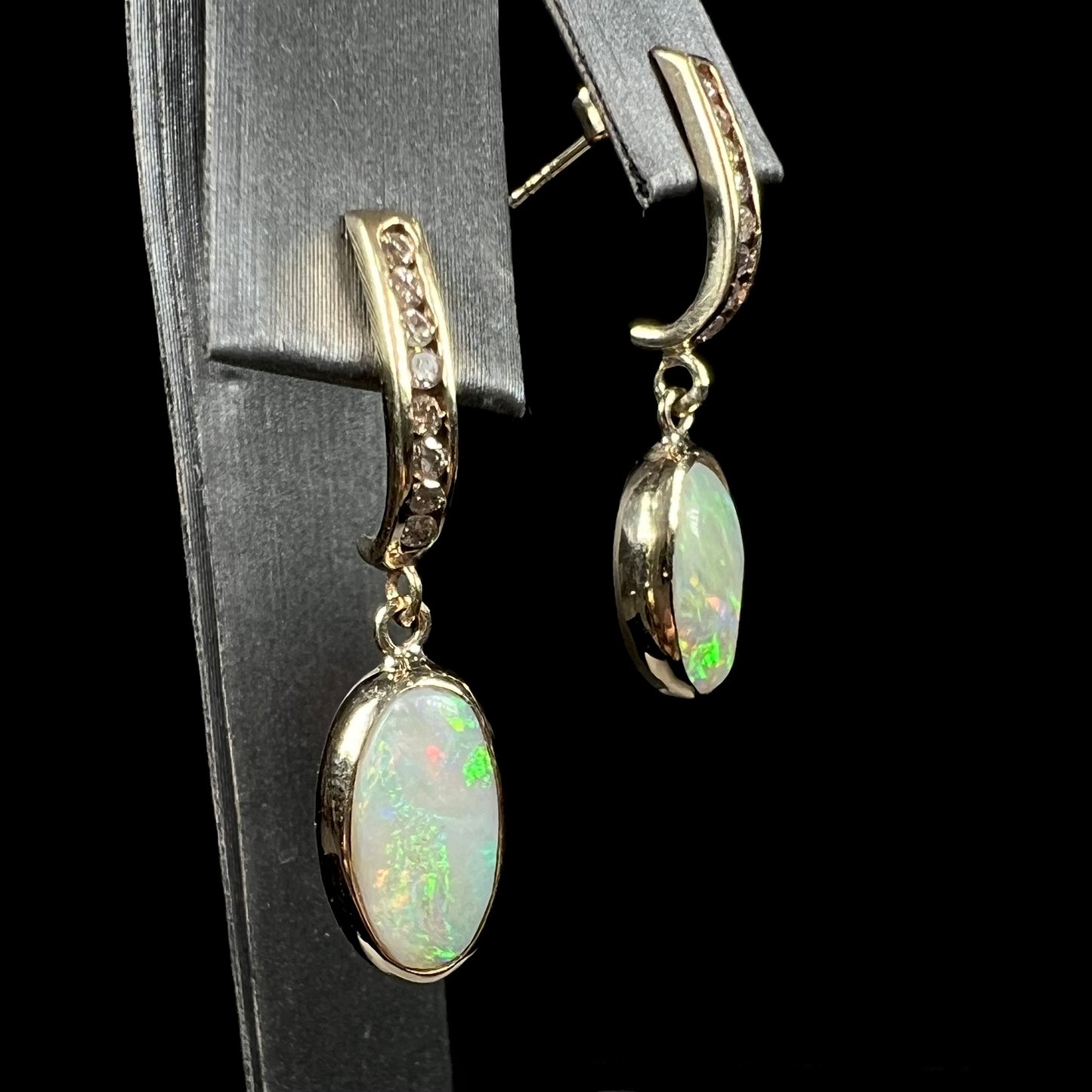 A pari of yellow gold dangle earrings set with natural white crystal opals and diamond accents.