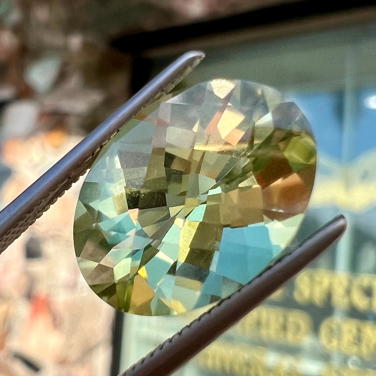 An oval checkerboard cut kiwi mystic topaz gemstone. The stone is a light yellowish green color.
