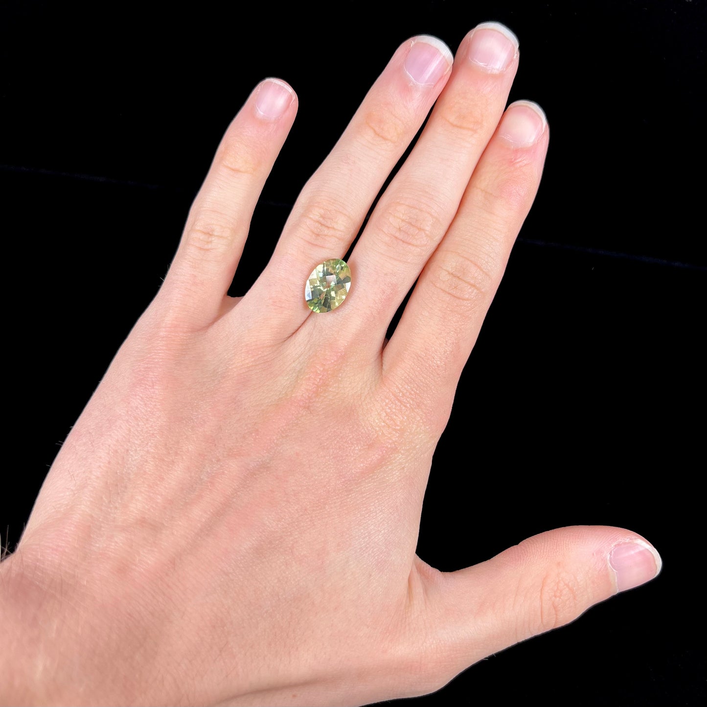 An oval checkerboard cut kiwi mystic topaz gemstone. The stone is a light yellowish green color.