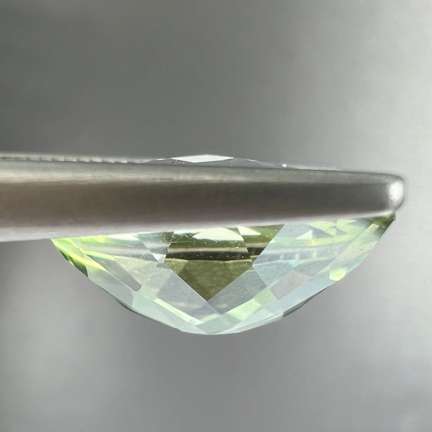 An oval checkerboard cut kiwi mystic topaz gemstone. The stone is a light yellowish green color.