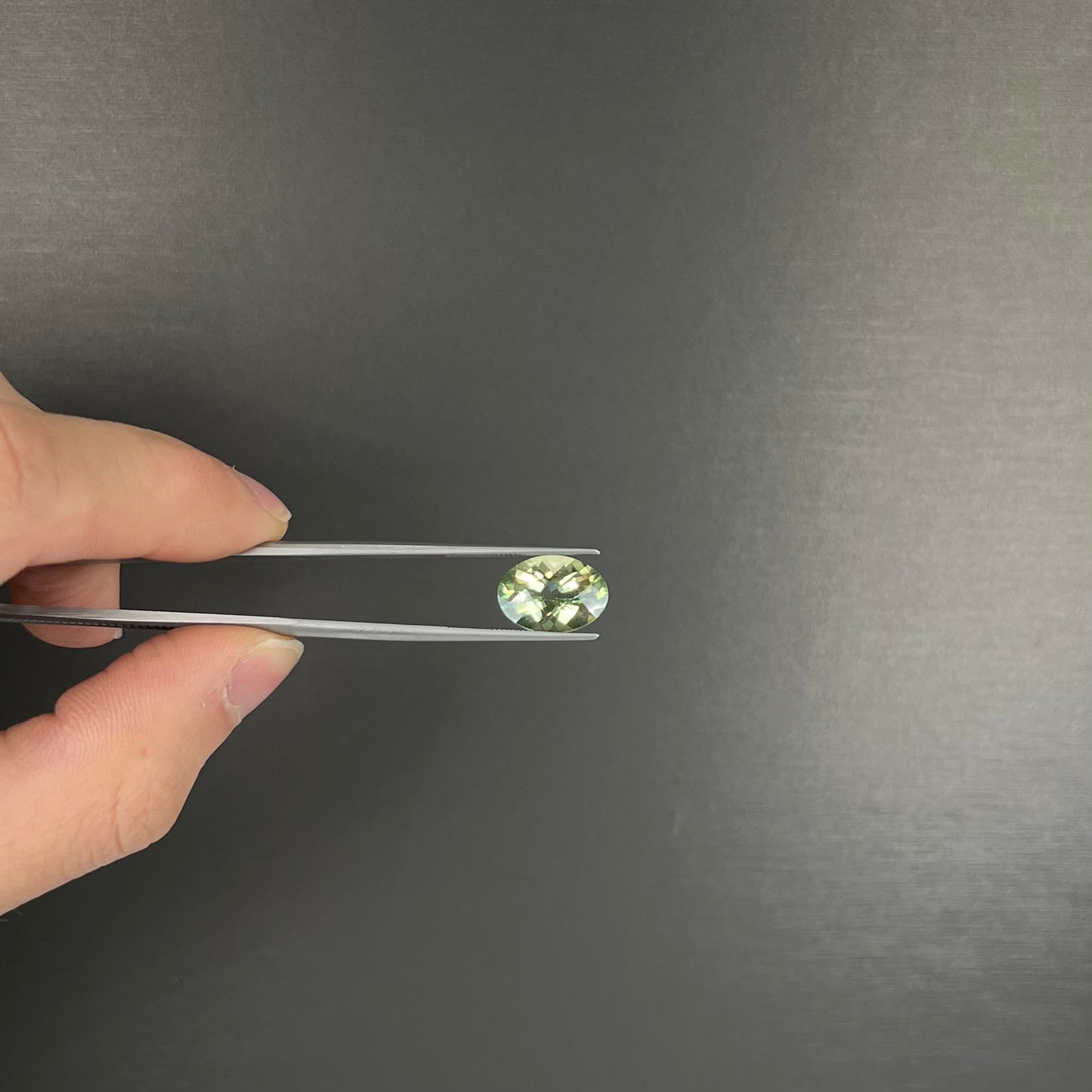 An oval checkerboard cut kiwi mystic topaz gemstone. The stone is a light yellowish green color.