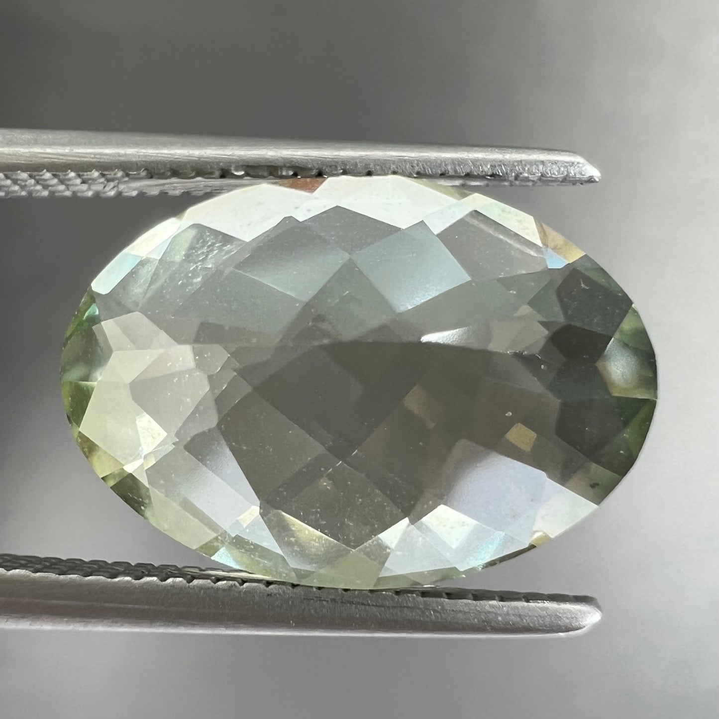 An oval checkerboard cut kiwi mystic topaz gemstone. The stone is a light yellowish green color.