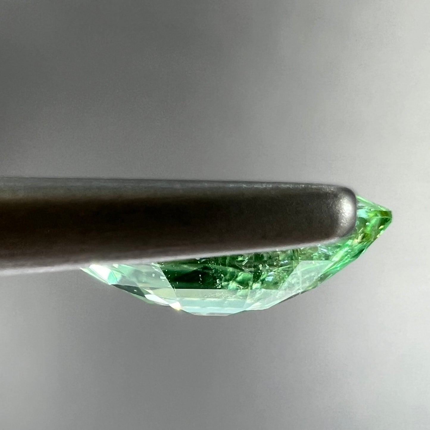 A faceted marquise cut electric green tourmaline gemstone. The stone has an eye-visible rutile needle inclusion.