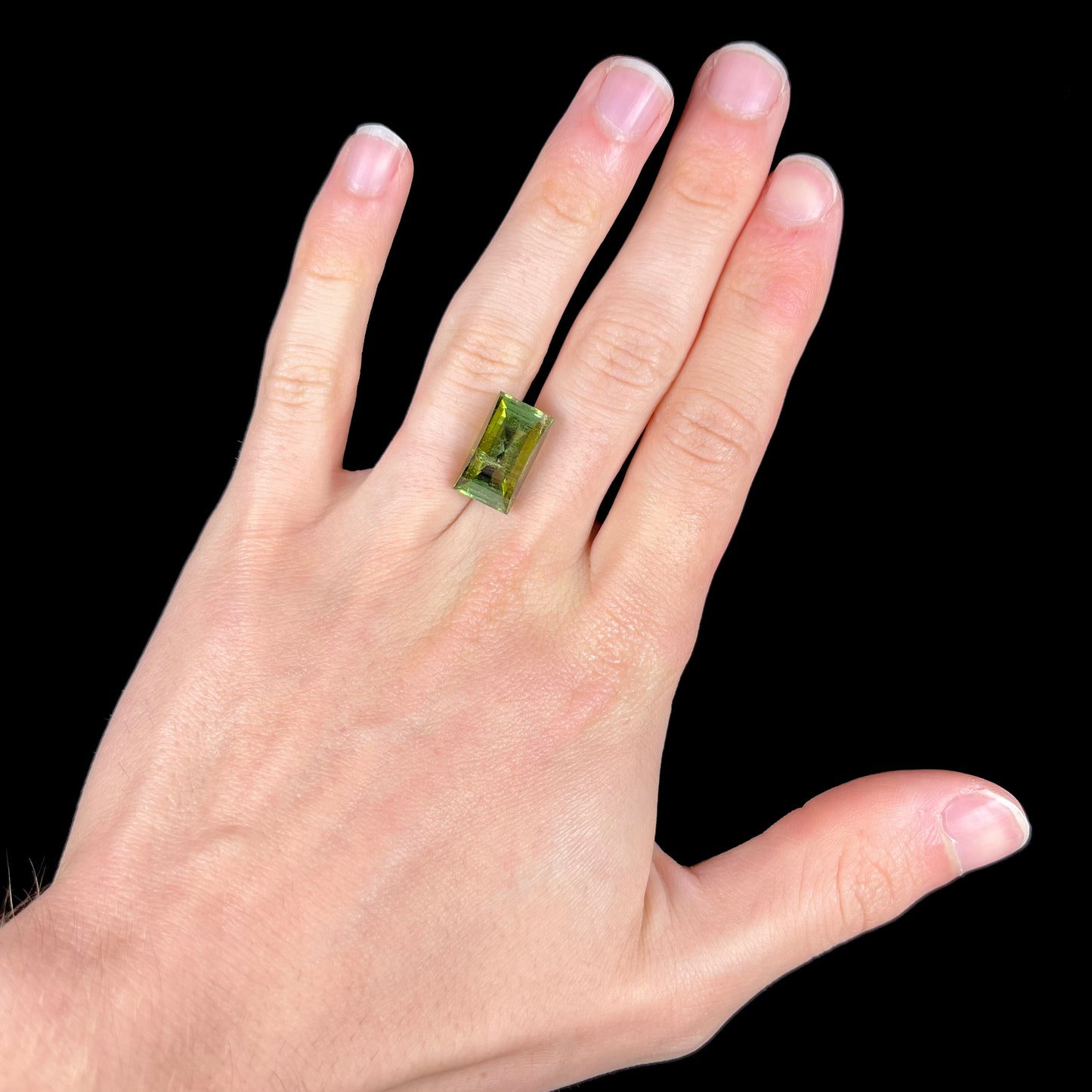 A rectangular step-cut yellowish green tourmaline gemstone.