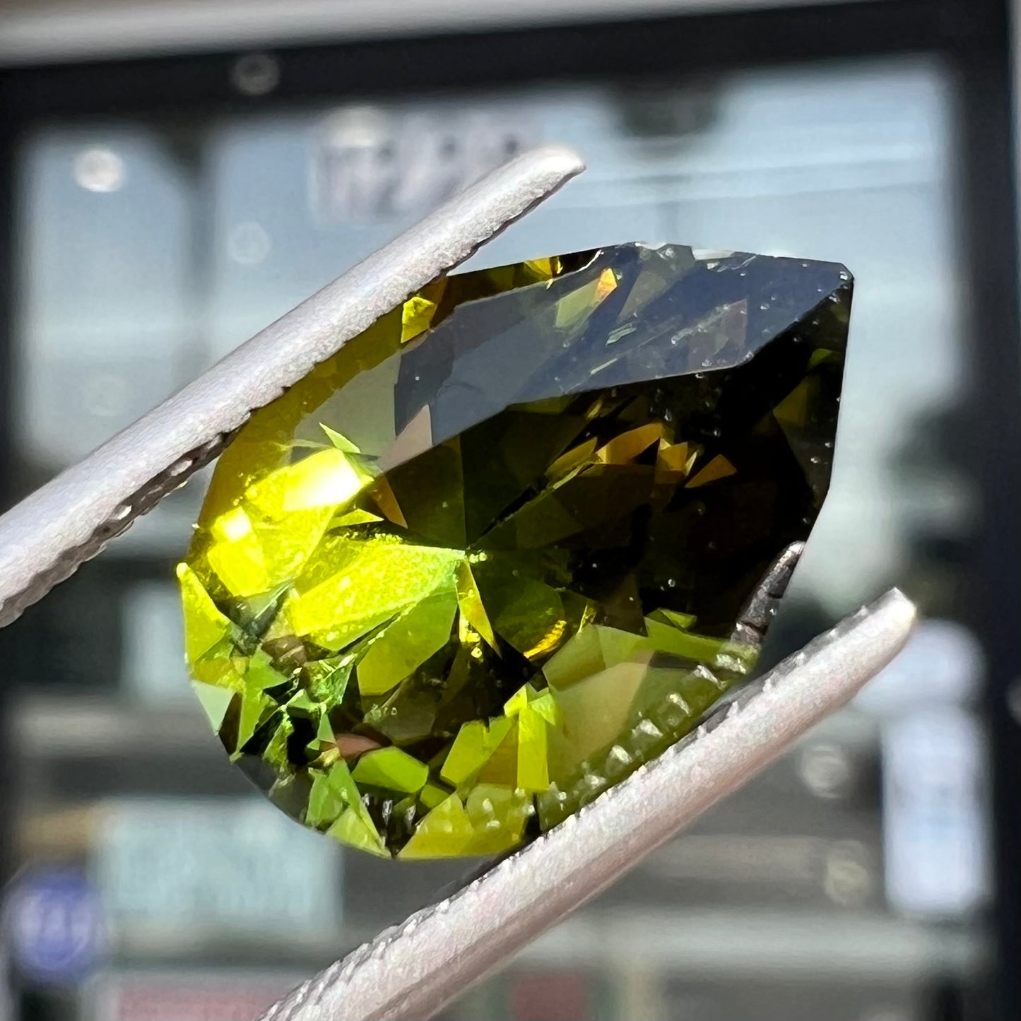 A loose, pear shaped green tourmaline gemstone. The color is dark green with a yellow secondary hue.