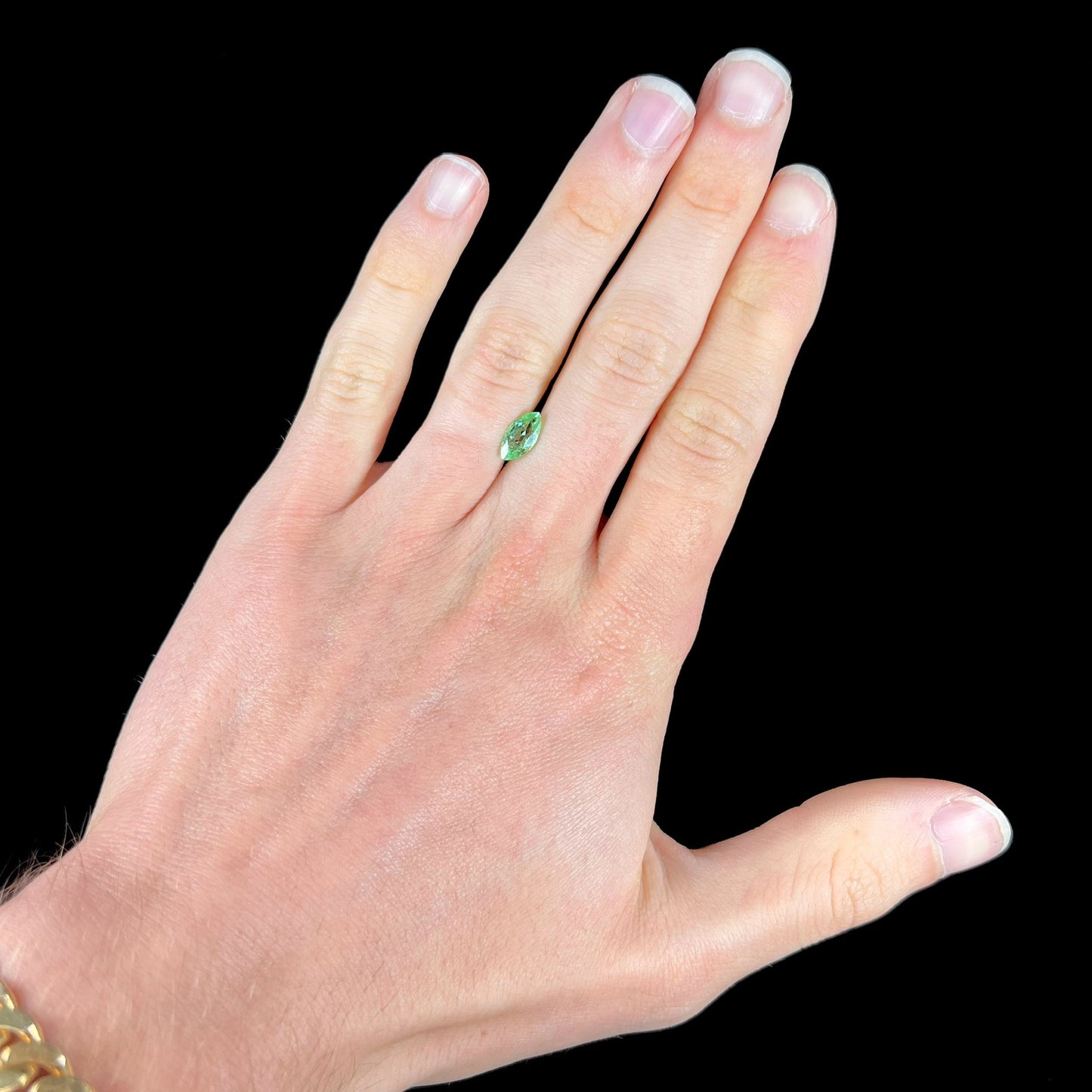 A faceted marquise cut electric green tourmaline gemstone. The stone has an eye-visible rutile needle inclusion.