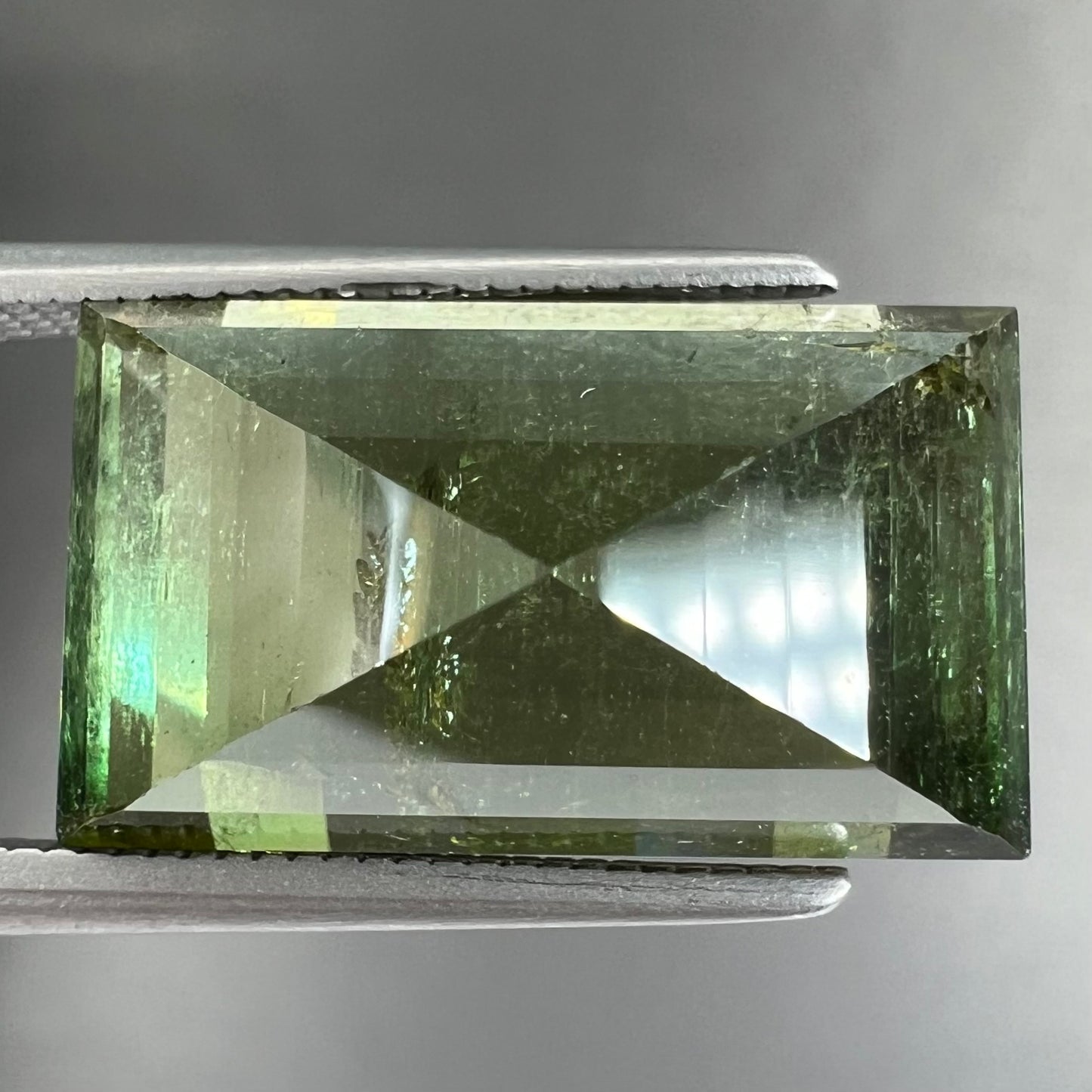A rectangular step-cut yellowish green tourmaline gemstone.