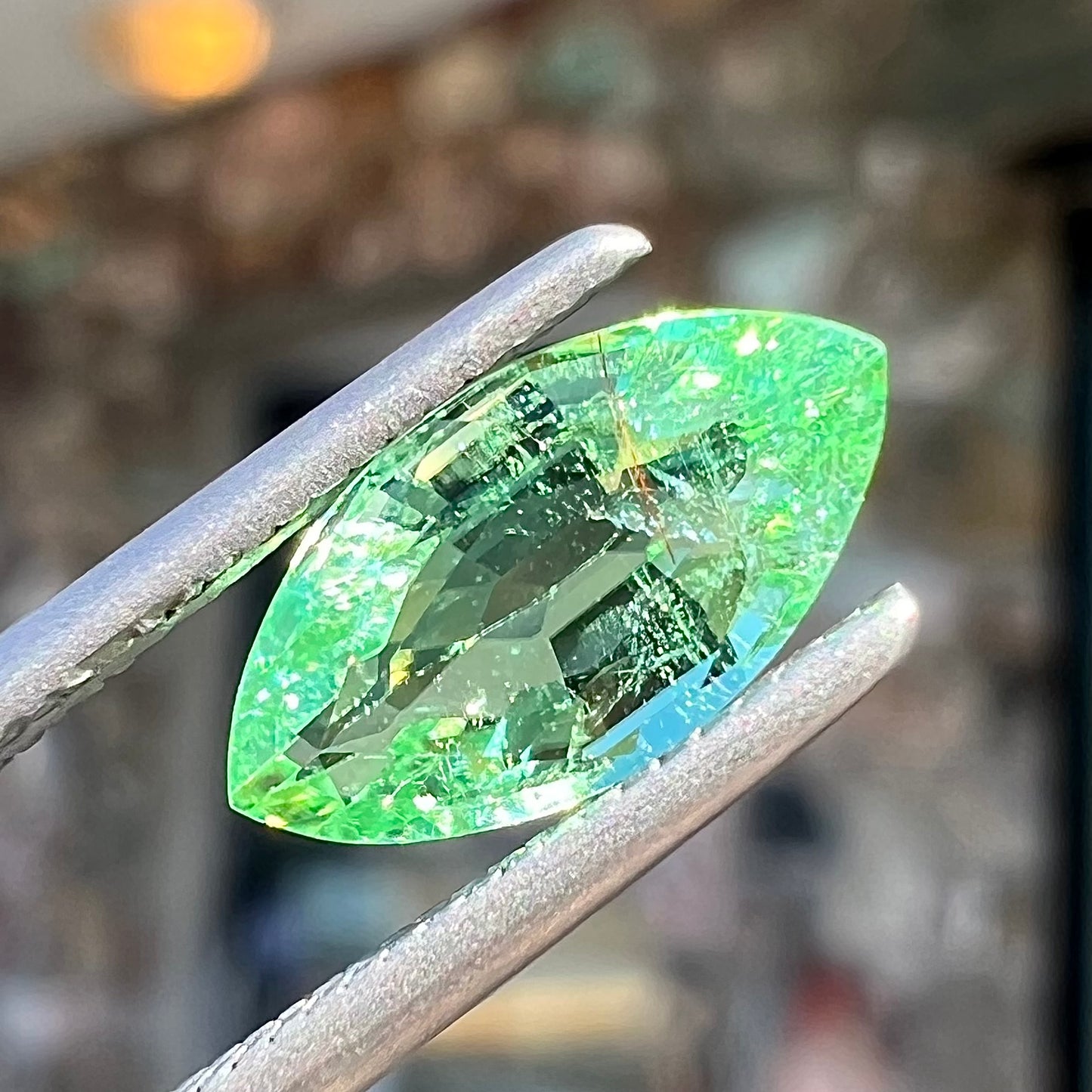 A faceted marquise cut electric green tourmaline gemstone. The stone has an eye-visible rutile needle inclusion.