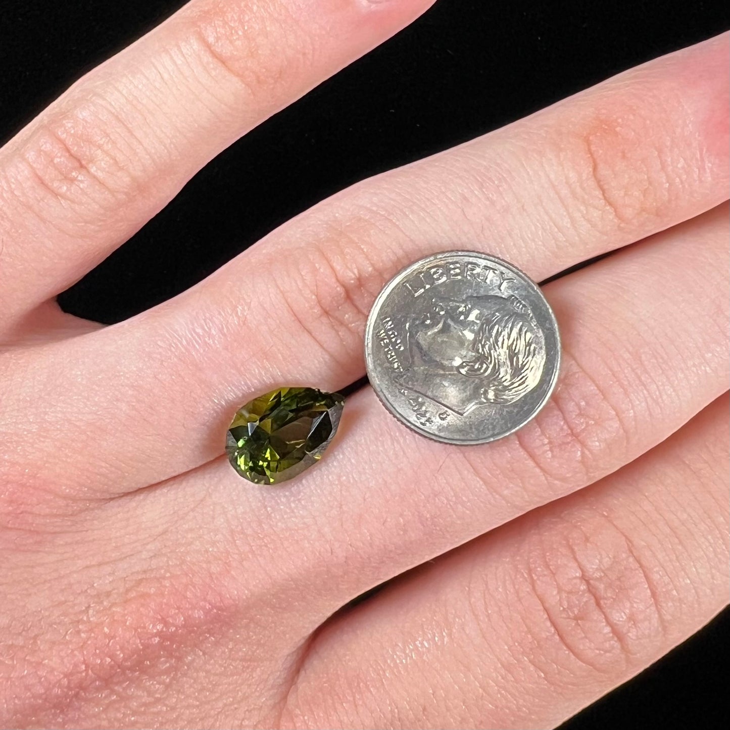 A loose, pear shaped green tourmaline gemstone. The color is dark green with a yellow secondary hue.