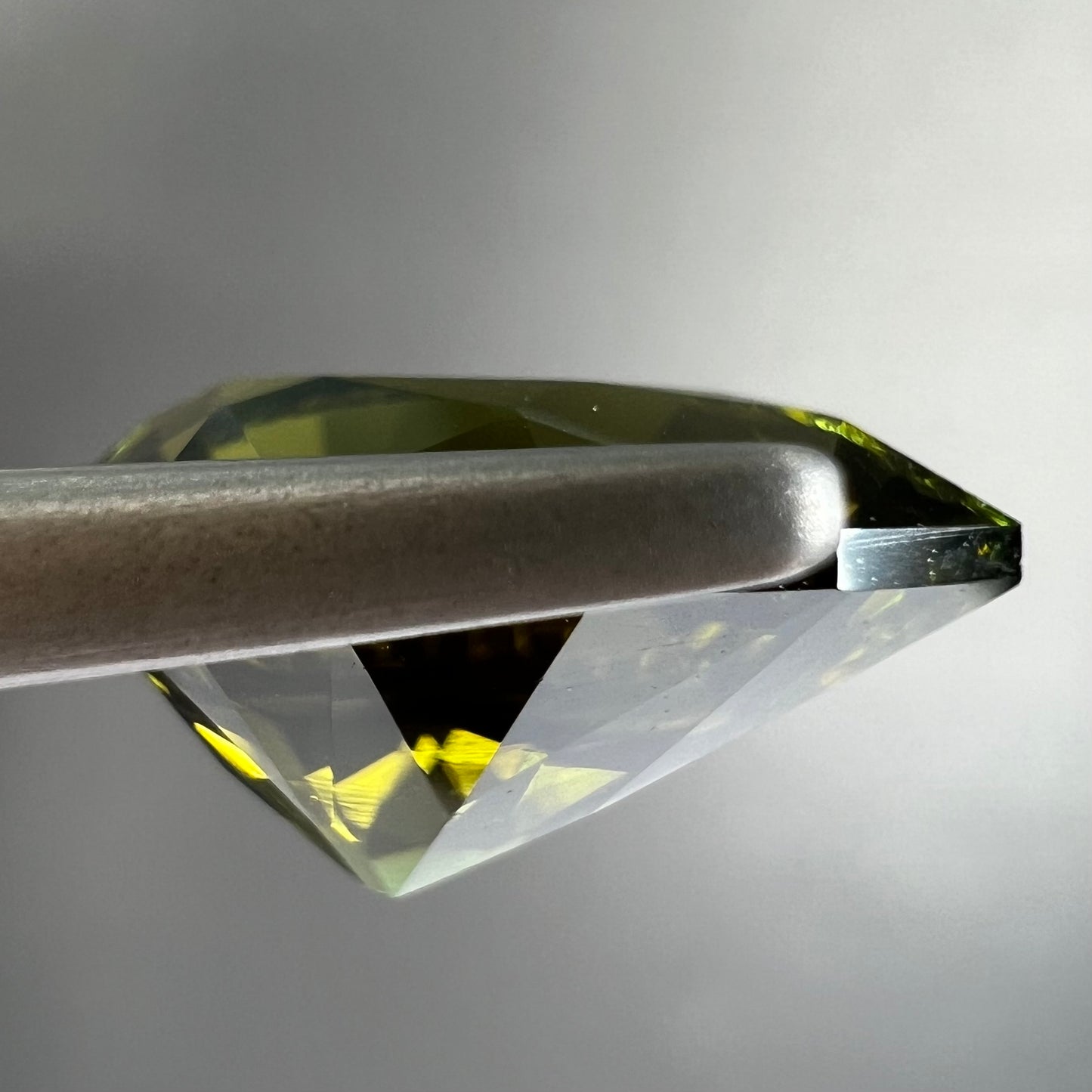 A loose, pear shaped green tourmaline gemstone. The color is dark green with a yellow secondary hue.