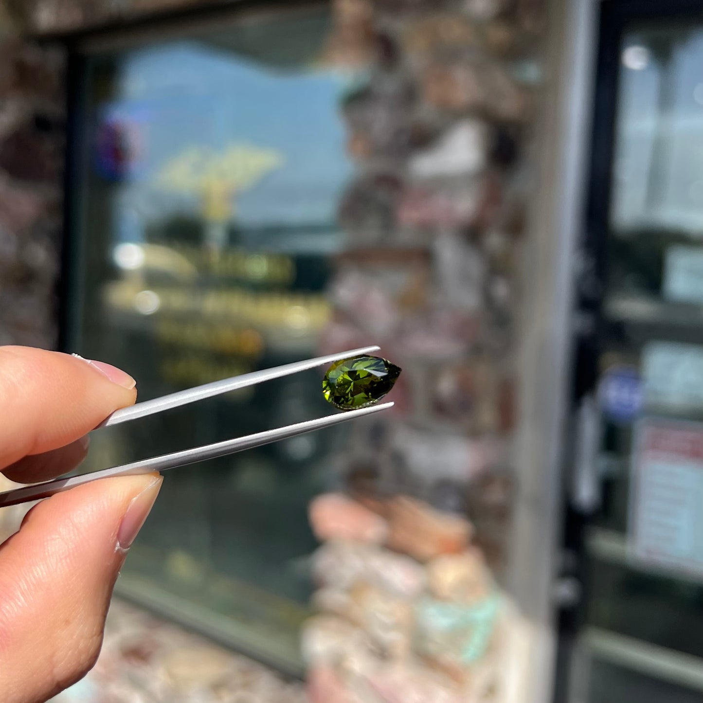 A loose, pear shaped green tourmaline gemstone. The color is dark green with a yellow secondary hue.