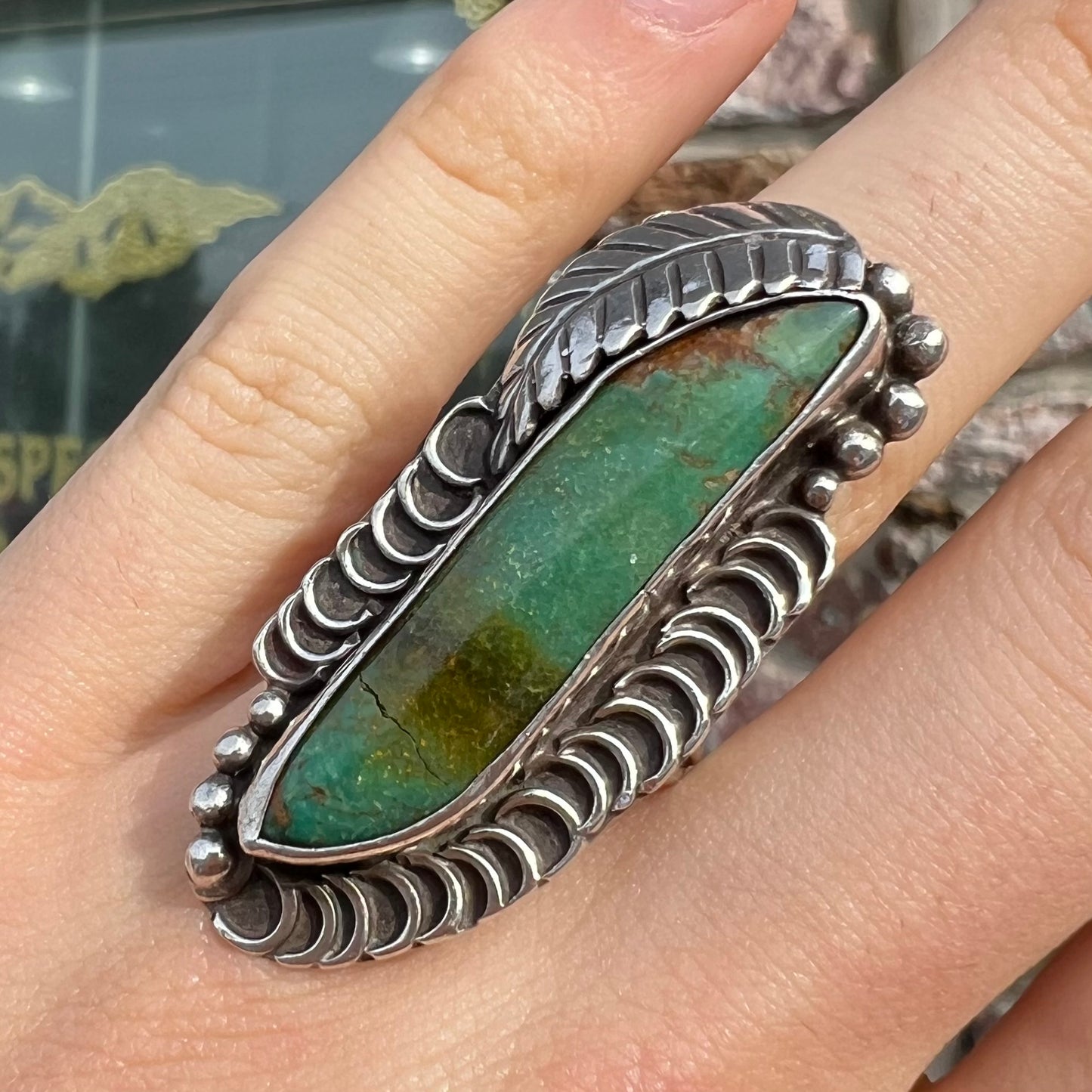 A sterling silver Navajo style ring set with a turquoise stone that shows colors of green, yellow, and reddish brown.
