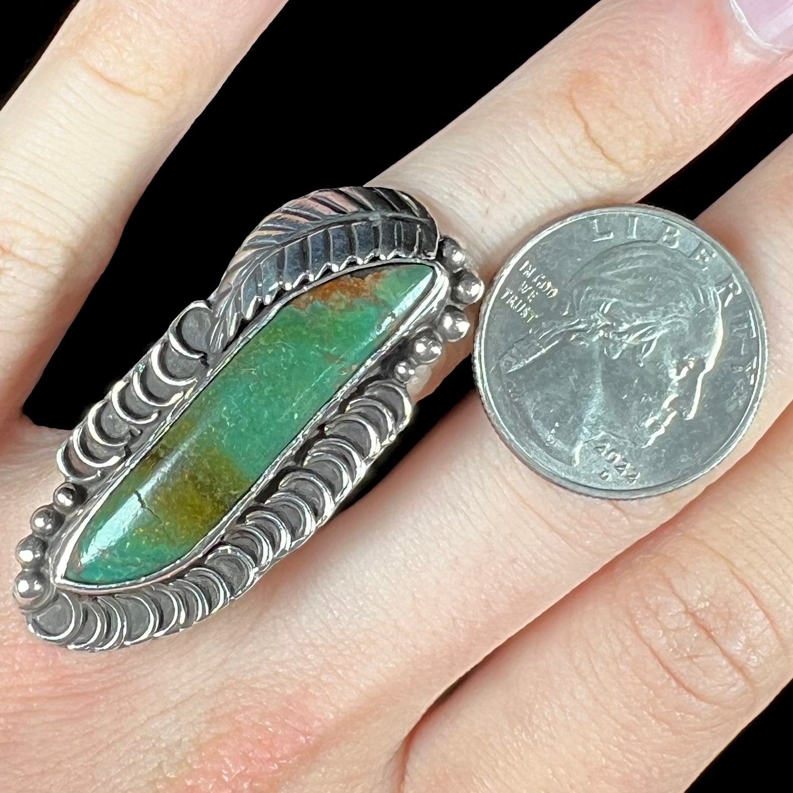 A sterling silver Navajo style ring set with a turquoise stone that shows colors of green, yellow, and reddish brown.