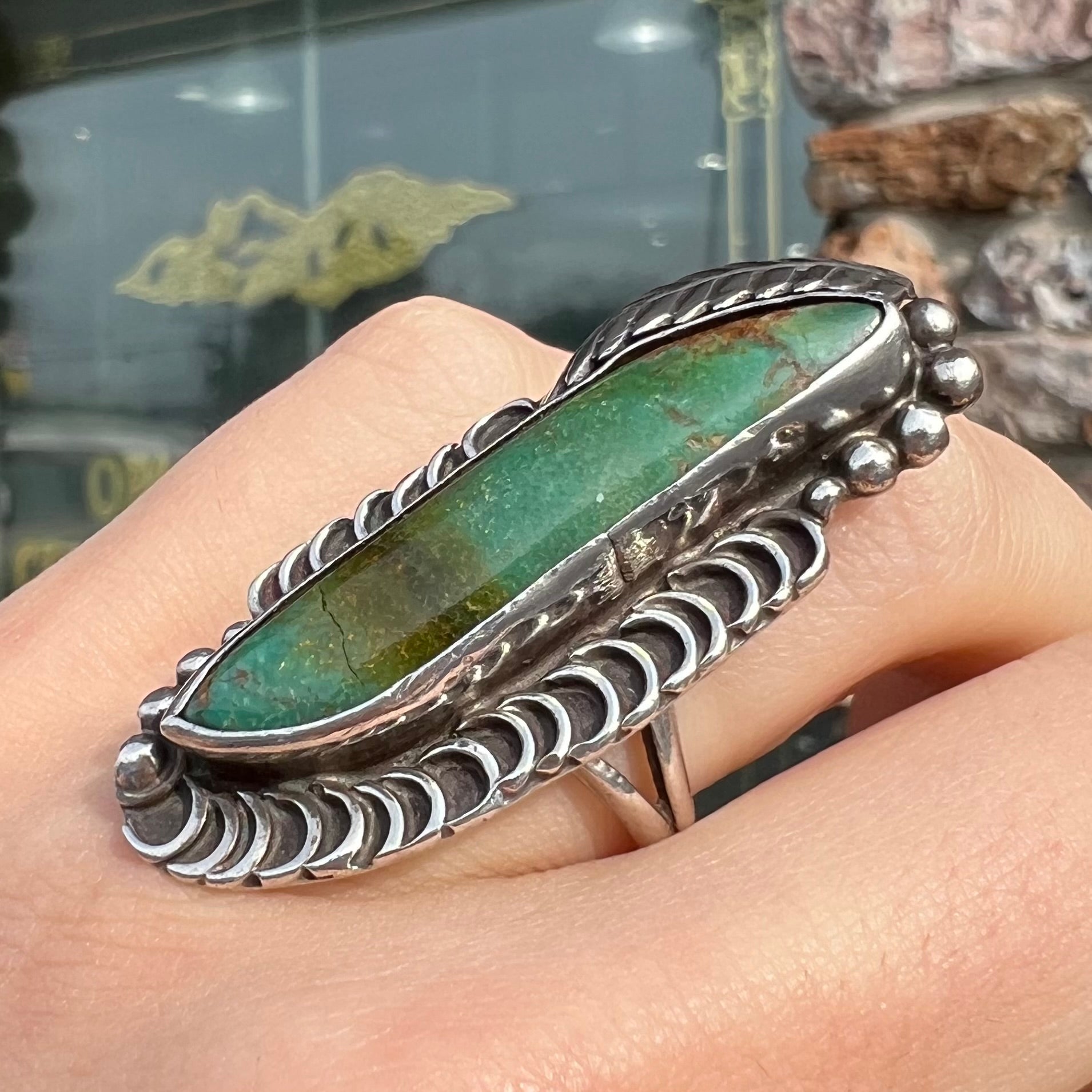 A sterling silver Navajo style ring set with a turquoise stone that shows colors of green, yellow, and reddish brown.