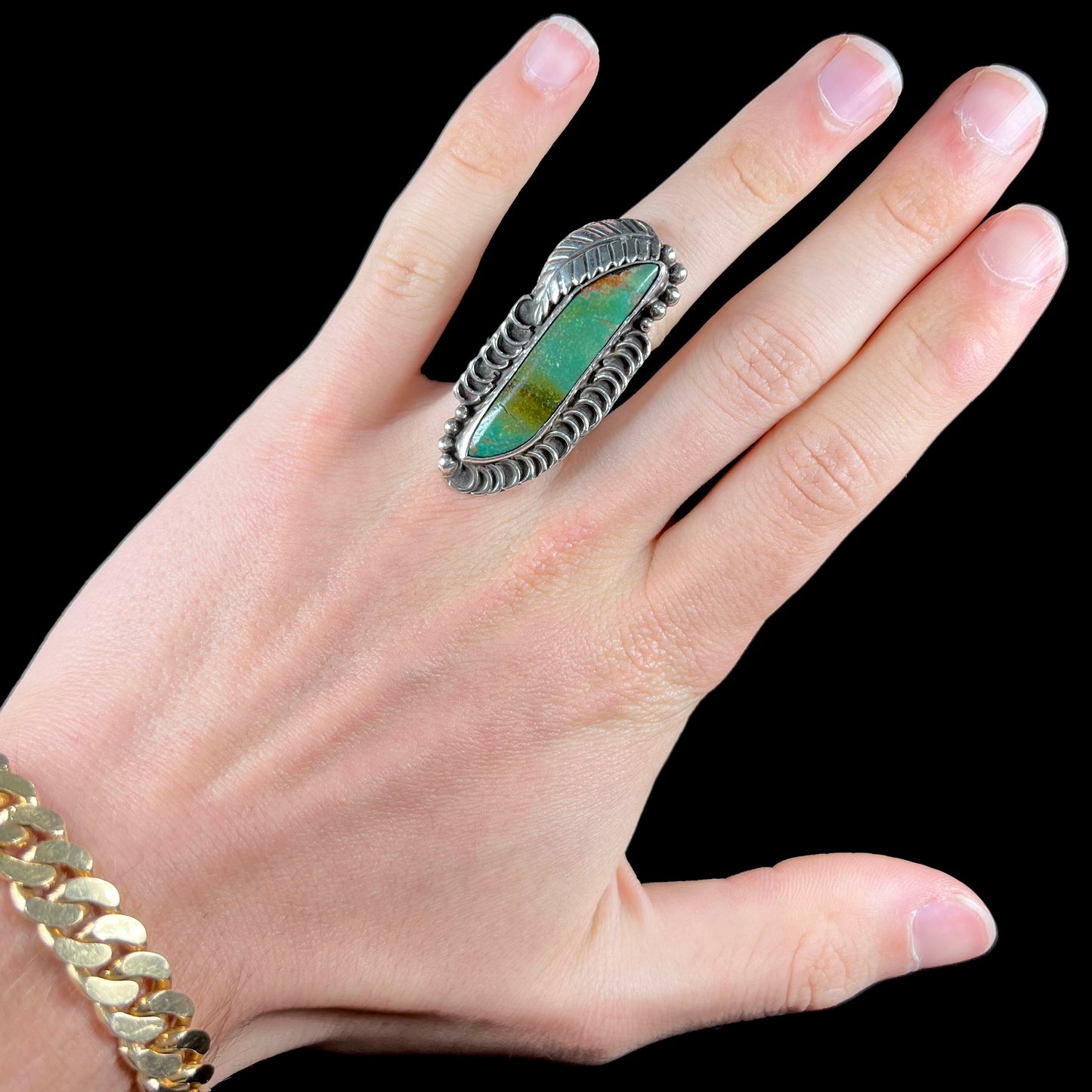 A sterling silver Navajo style ring set with a turquoise stone that shows colors of green, yellow, and reddish brown.
