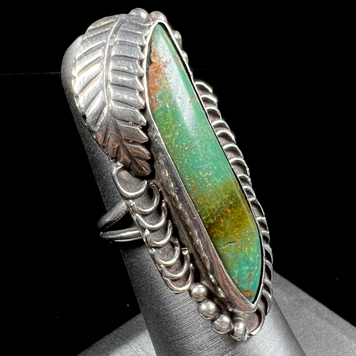 A sterling silver Navajo style ring set with a turquoise stone that shows colors of green, yellow, and reddish brown.