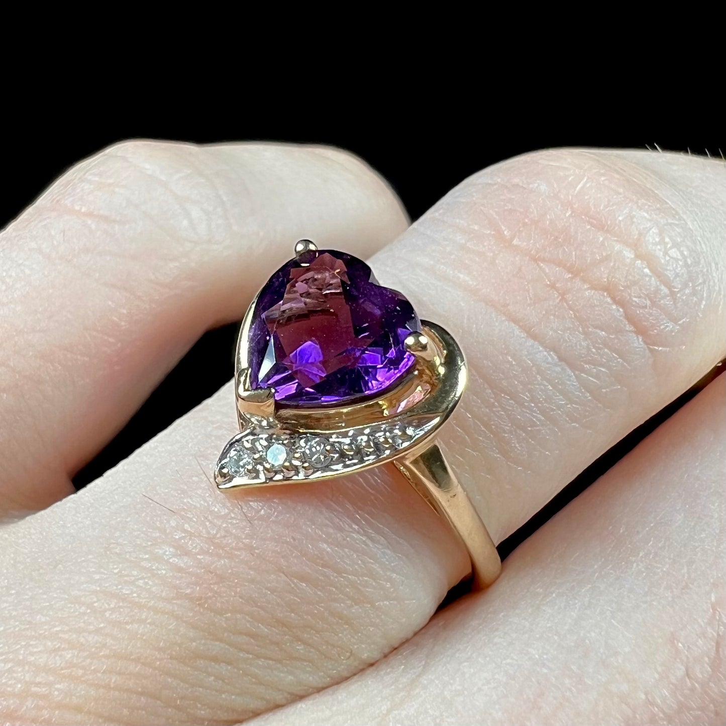 A ladies' yellow gold ring set with a heart shaped amethyst and round cut diamond accents.