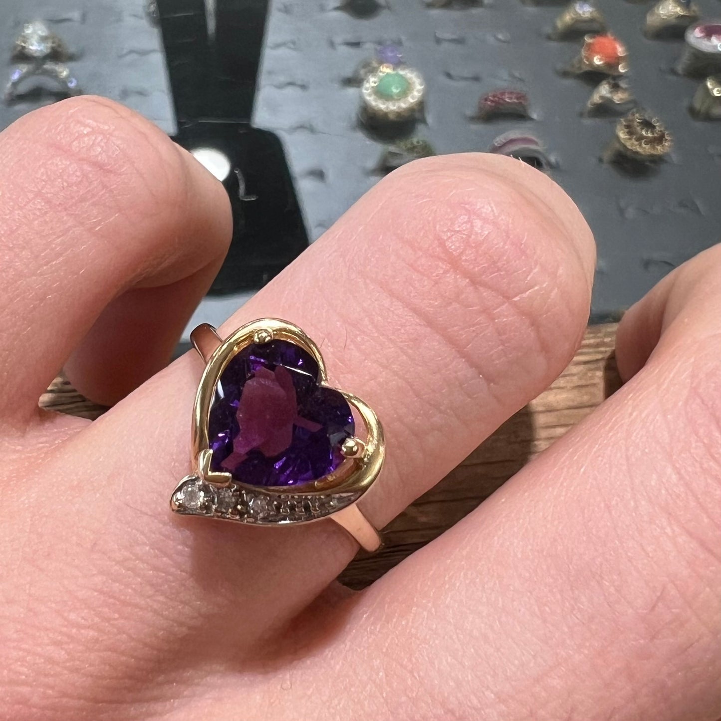 A ladies' yellow gold ring set with a heart shaped amethyst and round cut diamond accents.