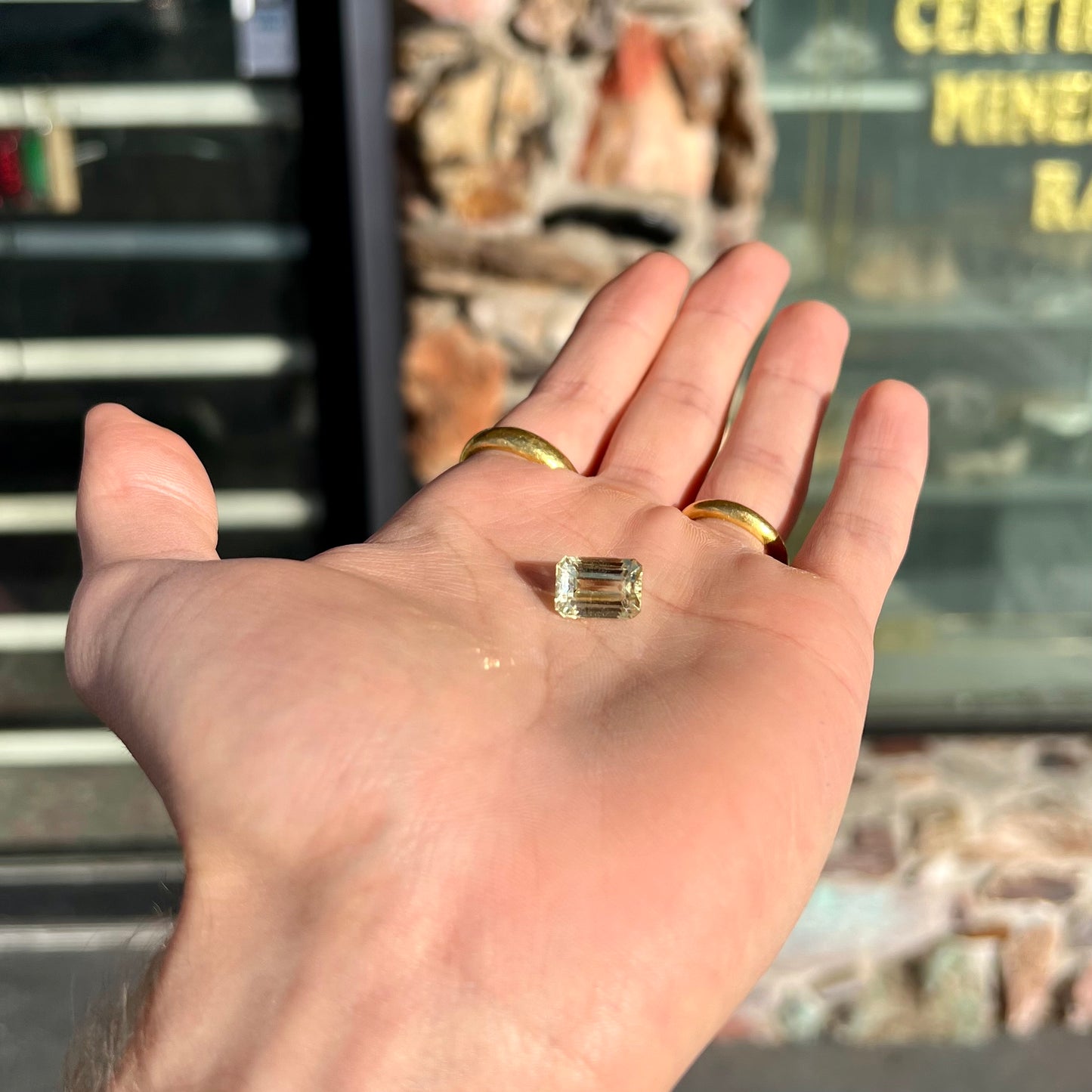 A loose, emerald cut hiddenite gemstone. The stone is a light yellow green color.