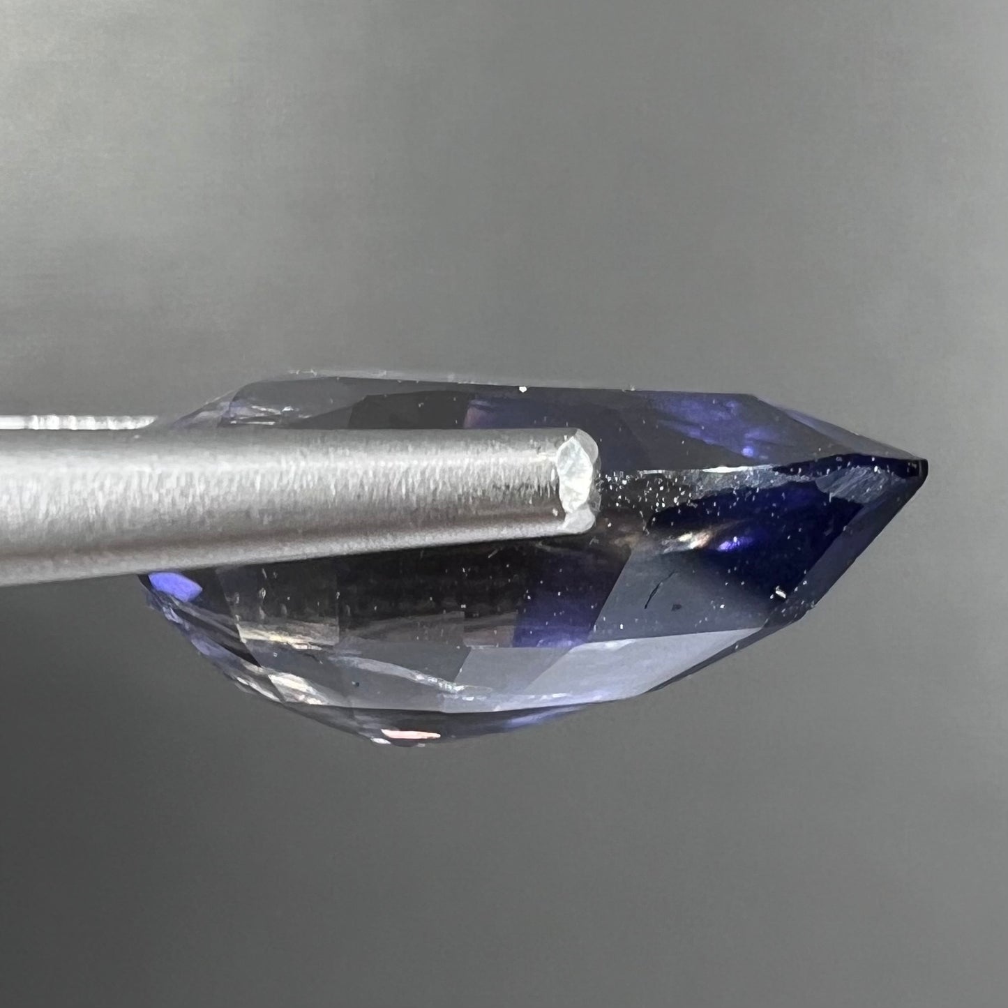 A loose, pear shaped bicolor iolite gemstone. The stone shows violite purple and silver colors.