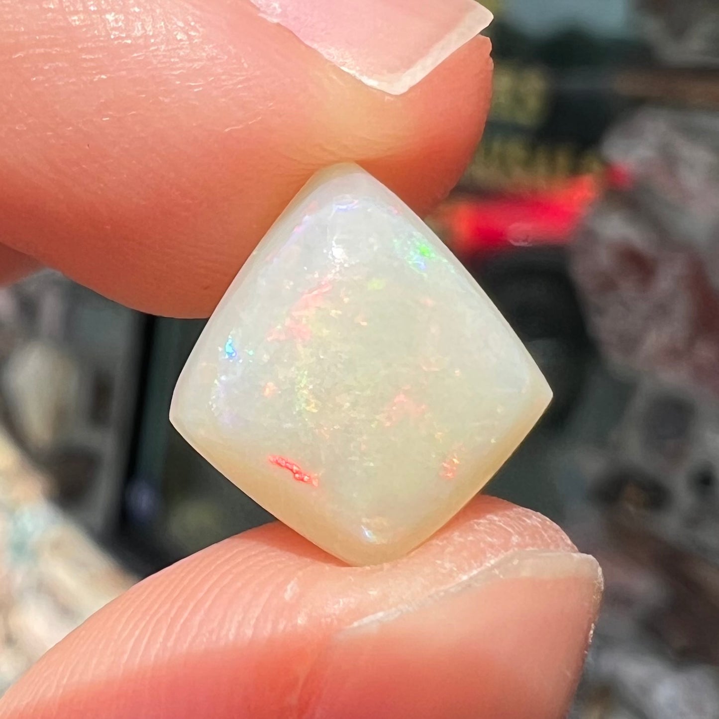 A loose, kite shaped white opal stone from Coober Pedy, Australia. The stone has subdued red colors.