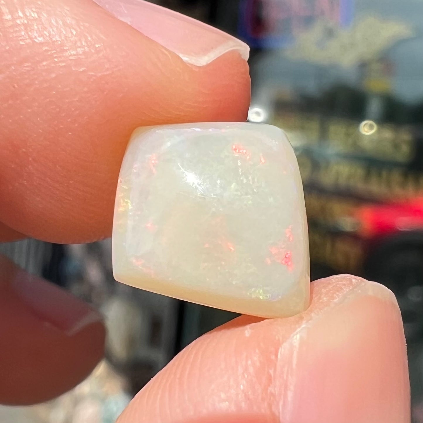 A loose, kite shaped white opal stone from Coober Pedy, Australia. The stone has subdued red colors.