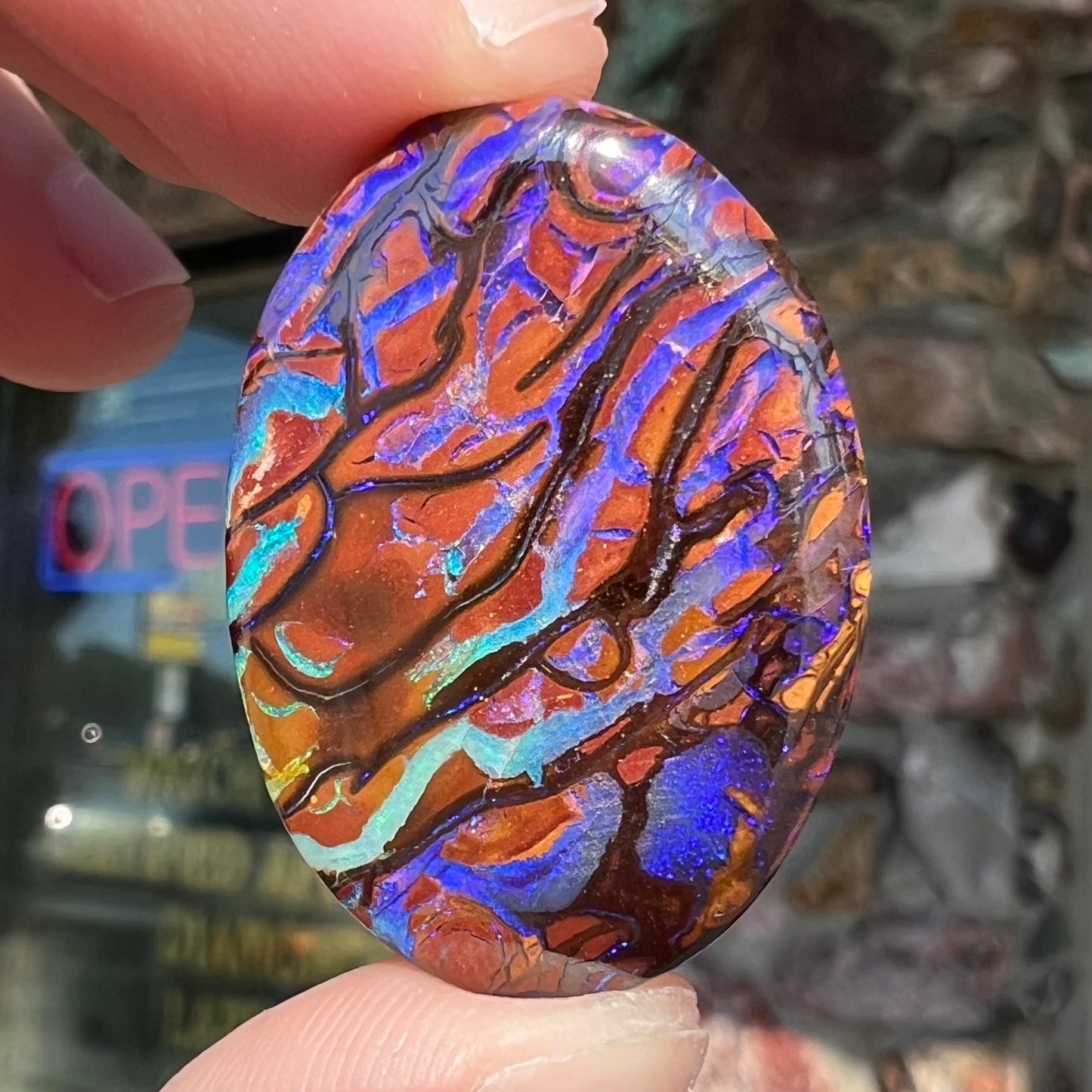 A loose, oval cabochon cut boulder opal from Koroit, Australia. The opal has violet and purple veins.