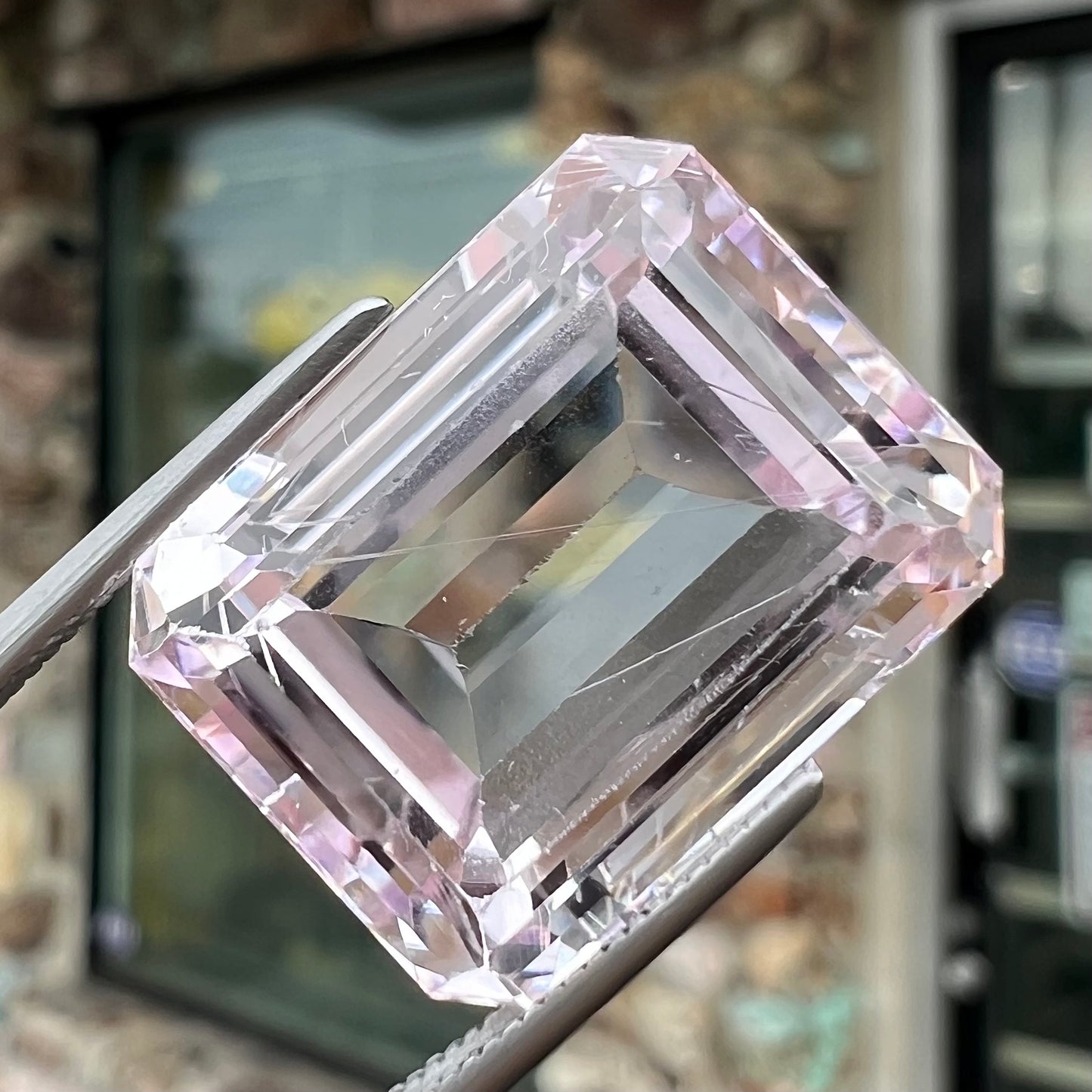 A loose, emerald cut kunzite gemstone. The stone has eye-visible rutile needle inclusions and the table is abraded.