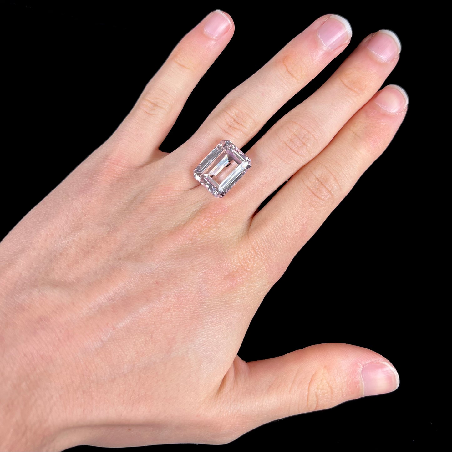A loose, emerald cut kunzite gemstone. The stone has eye-visible rutile needle inclusions and the table is abraded.