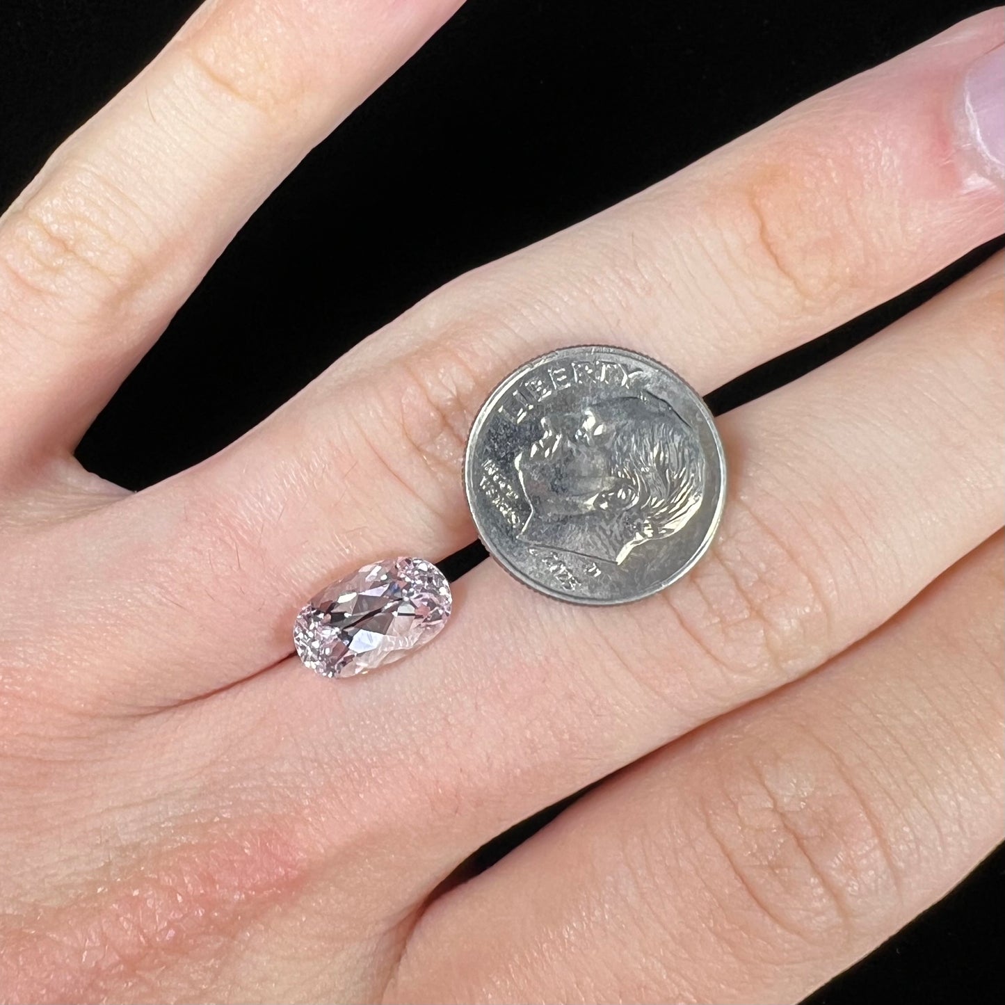 A loose, faceted oval cut kunzite gemstone. The stone is a light pink color.
