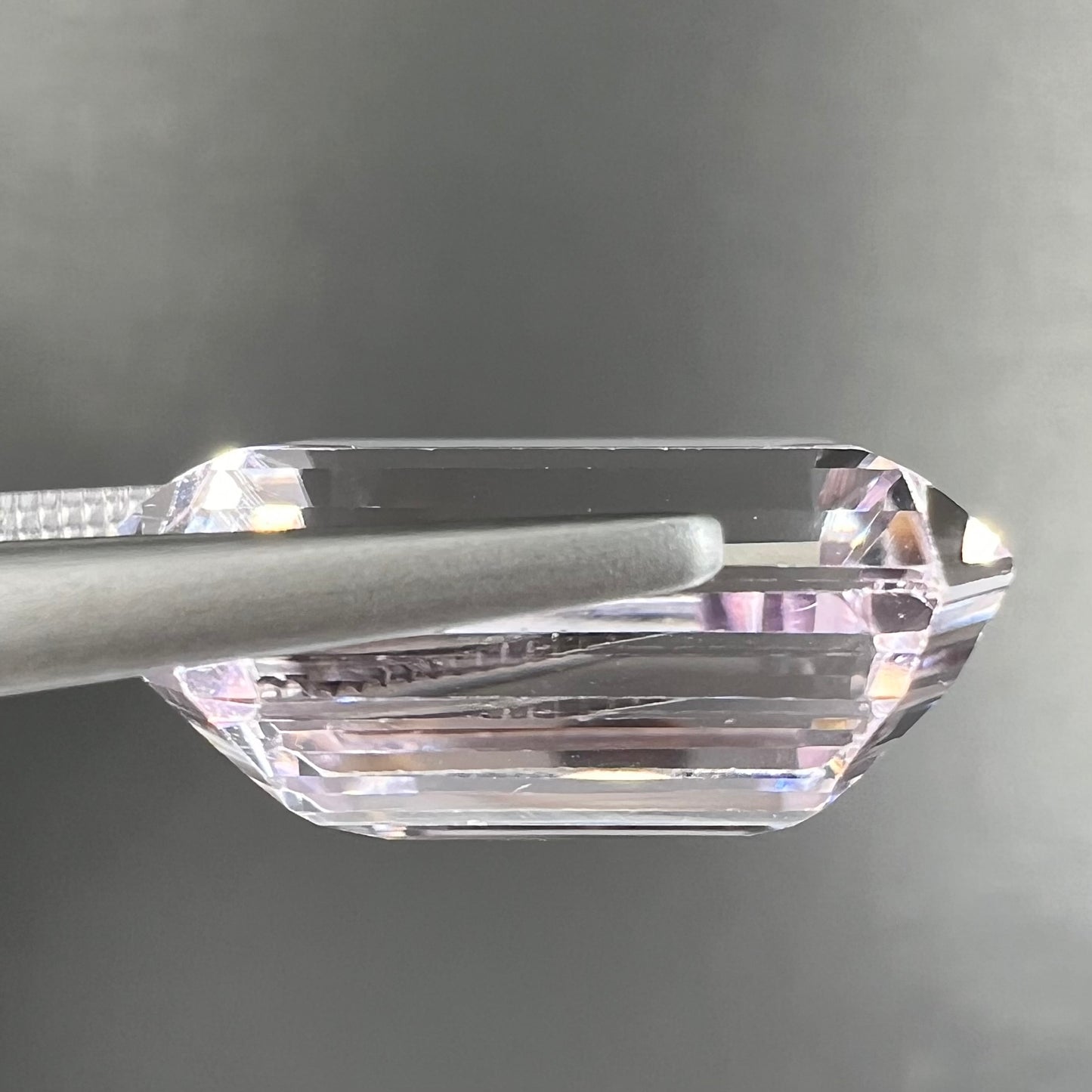 A loose, emerald cut kunzite gemstone. The stone has eye-visible rutile needle inclusions and the table is abraded.