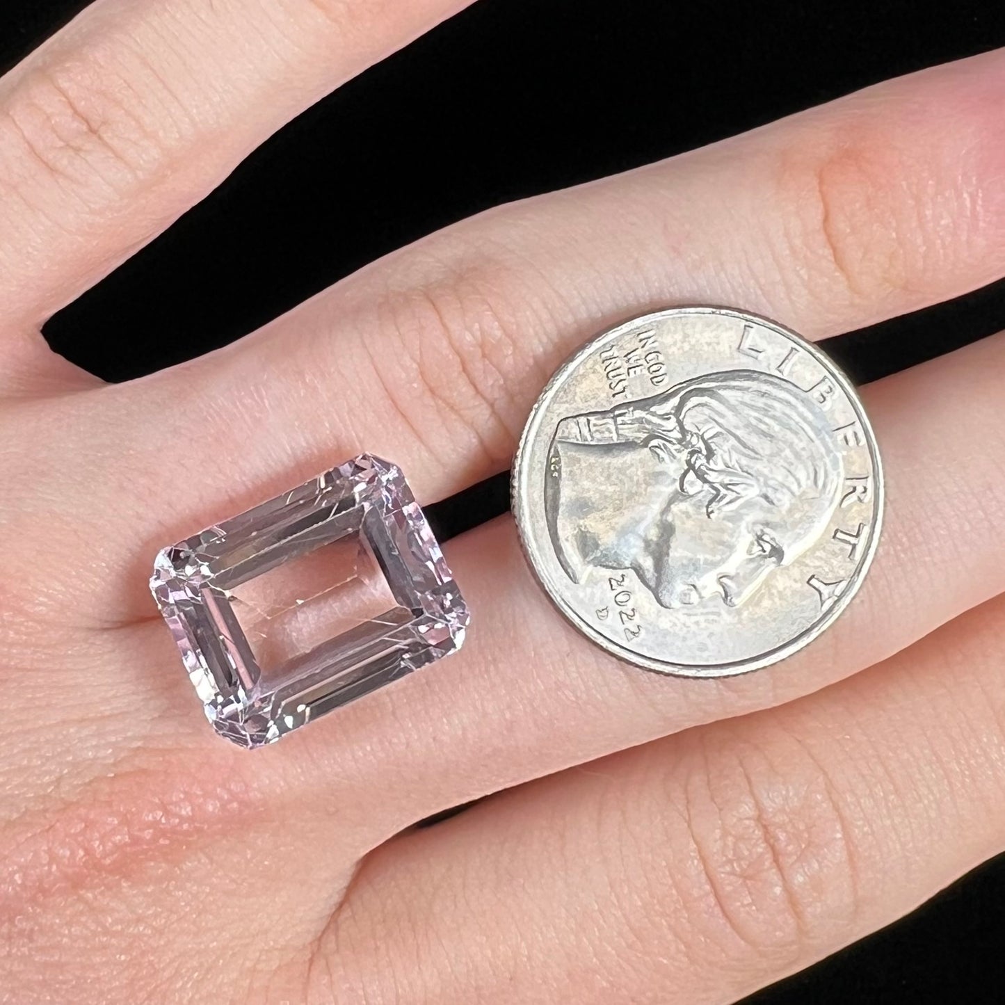 A loose, emerald cut kunzite gemstone. The stone has eye-visible rutile needle inclusions and the table is abraded.