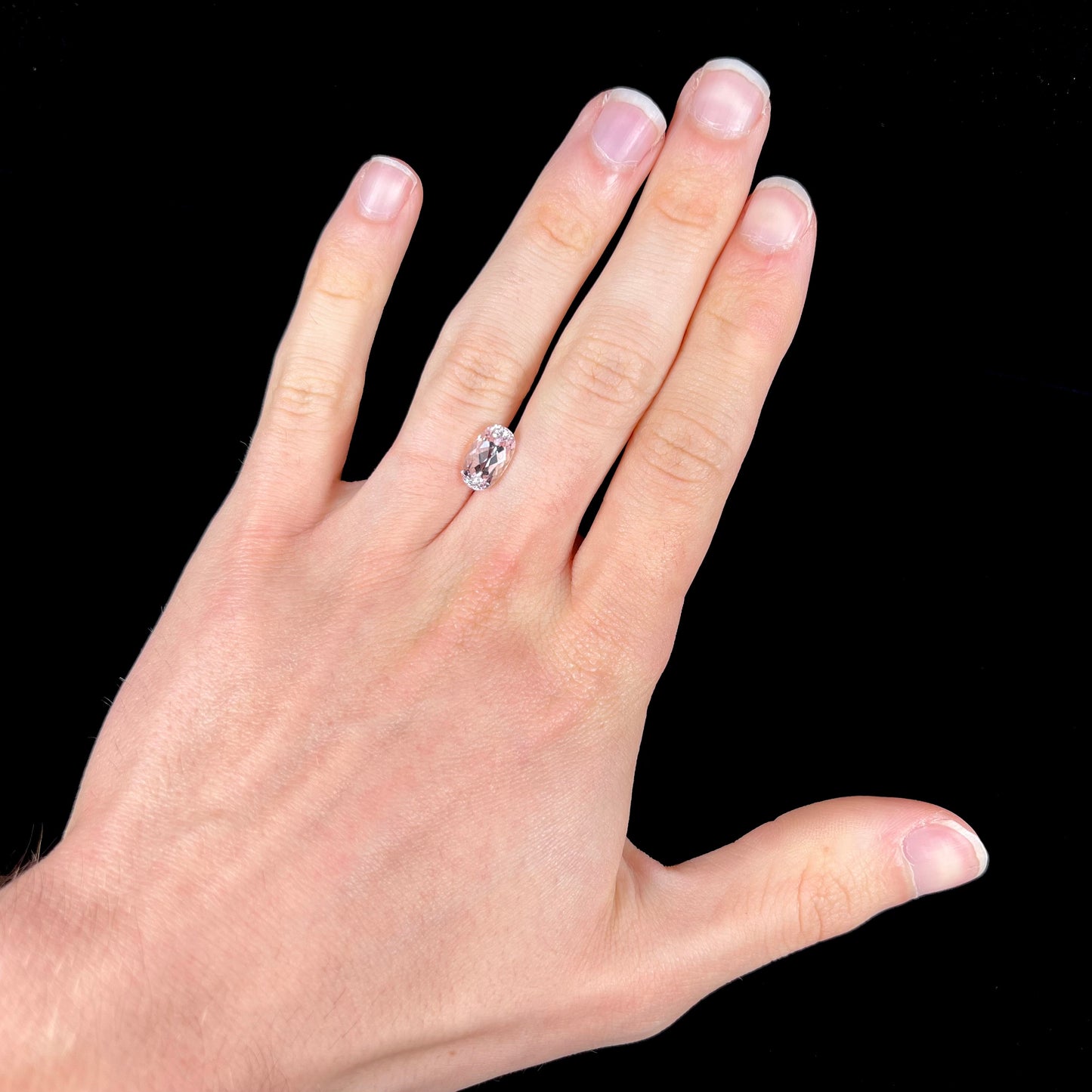 A loose, faceted oval cut kunzite gemstone. The stone is a light pink color.