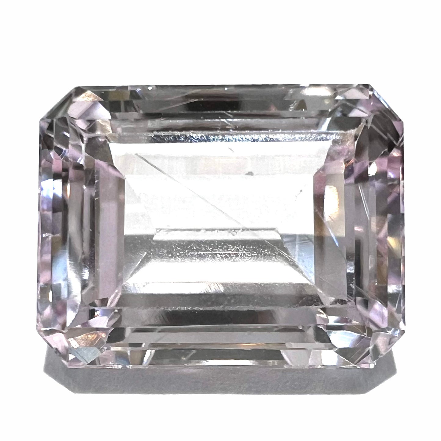 A loose, emerald cut kunzite gemstone. The stone has eye-visible rutile needle inclusions and the table is abraded.