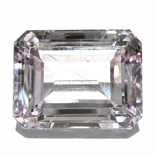 A loose, emerald cut kunzite gemstone.  The stone has eye-visible rutile needle inclusions and the table is abraded.