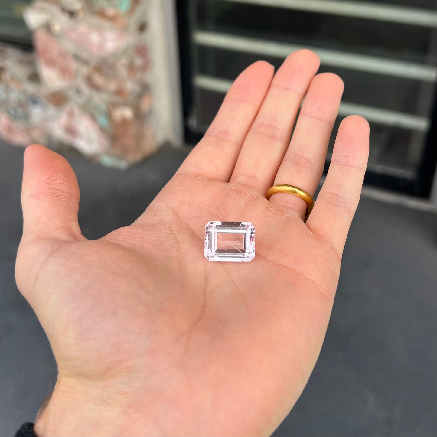 A loose, emerald cut kunzite gemstone. The stone has eye-visible rutile needle inclusions and the table is abraded.