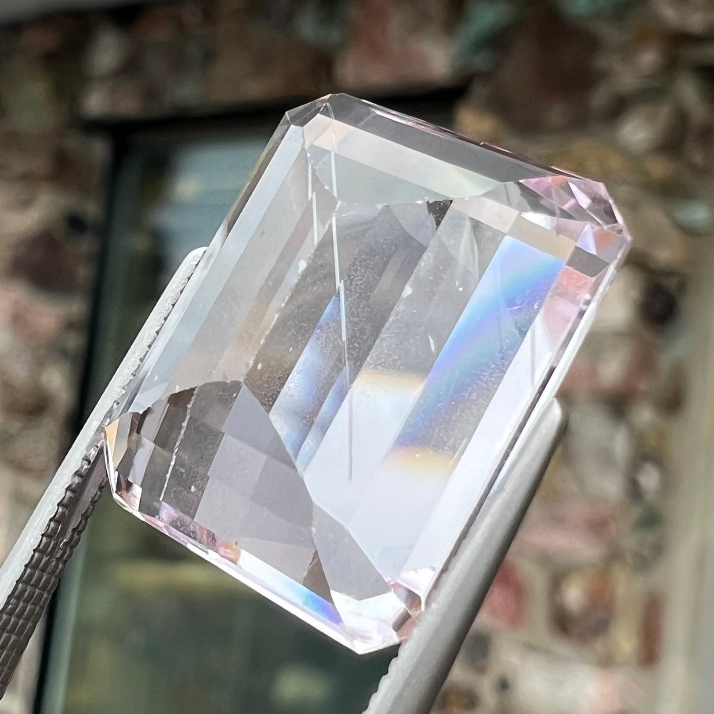 A loose, emerald cut kunzite gemstone. The stone has eye-visible rutile needle inclusions and the table is abraded.