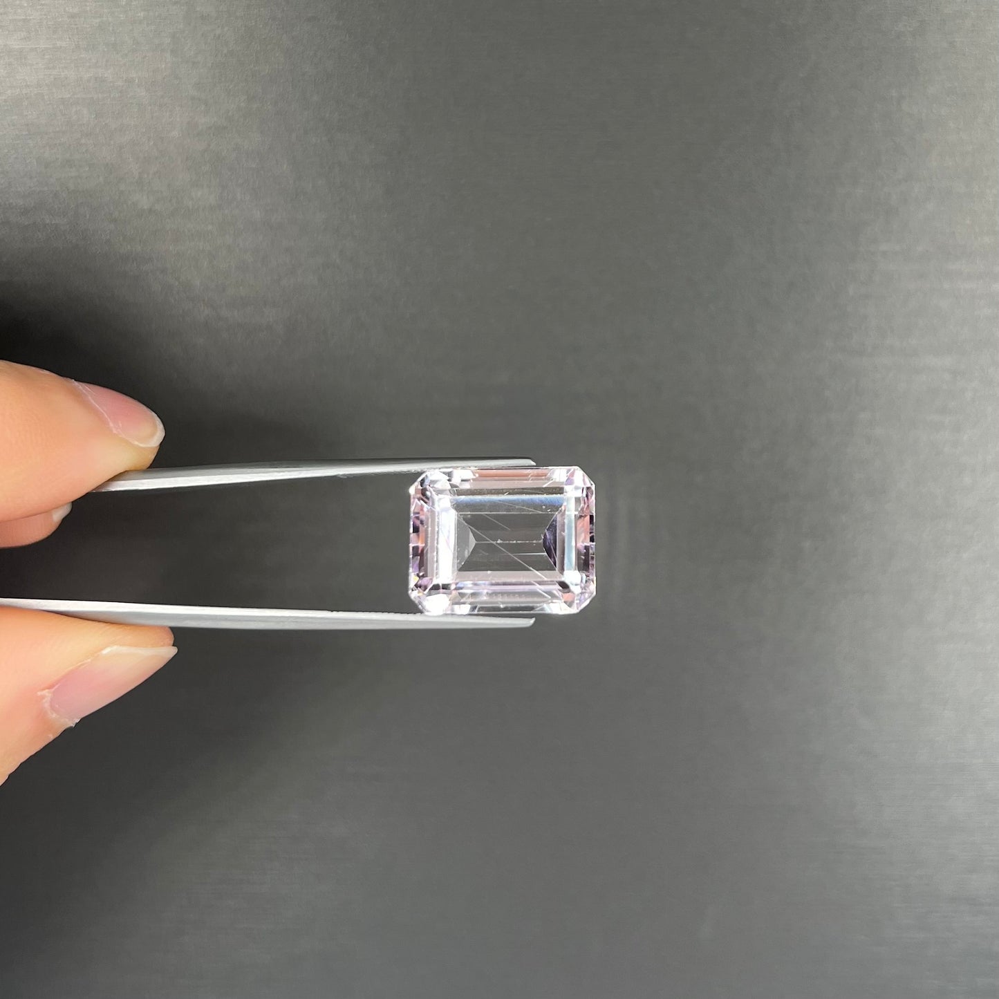 A loose, emerald cut kunzite gemstone. The stone has eye-visible rutile needle inclusions and the table is abraded.