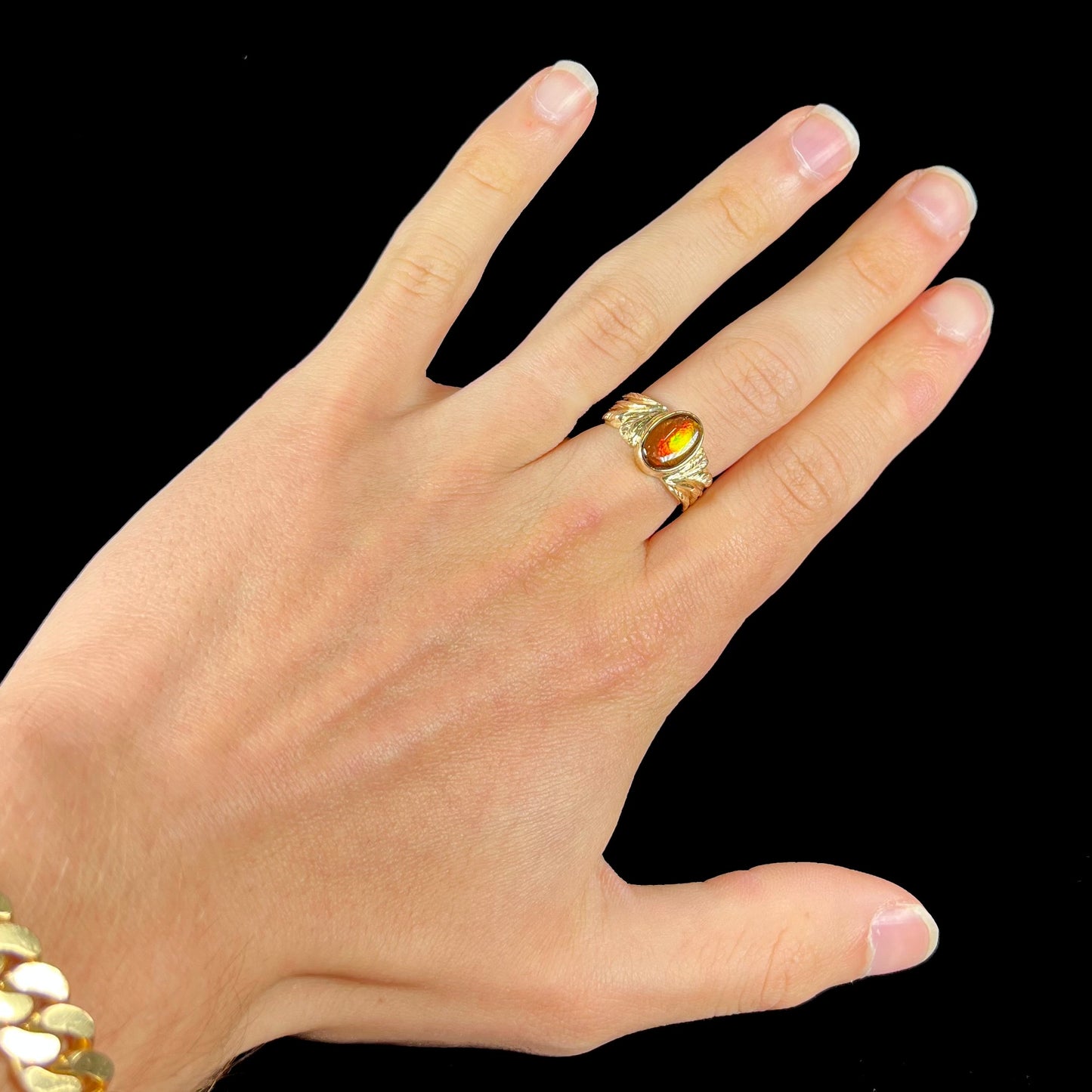 A unisex oval cabochon cut fire agate ring cast in yellow gold. The stone flashes green and red colors.