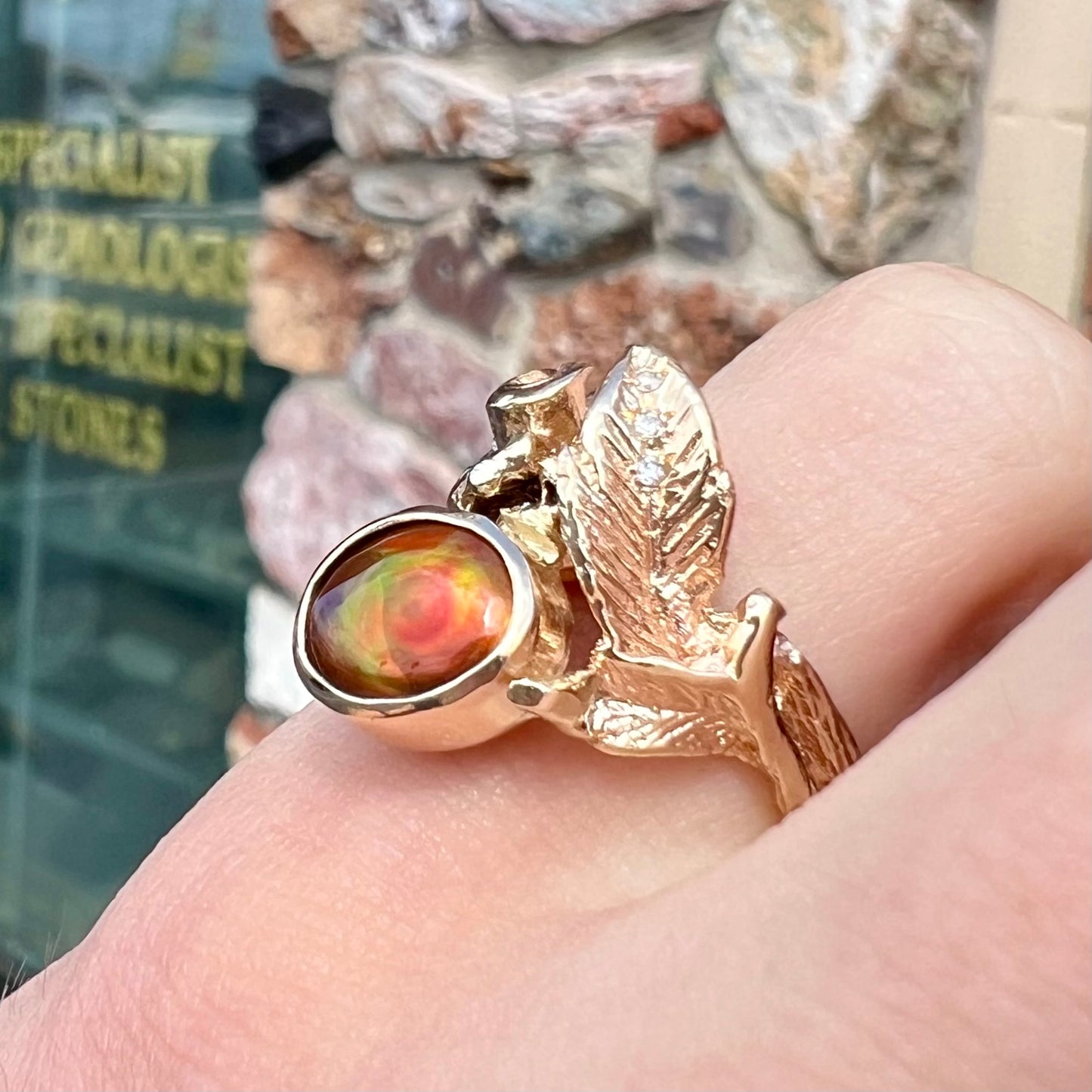 A ladies' yellow gold flower style ring set with an oval cabochon cut fire agate and diamond accents.