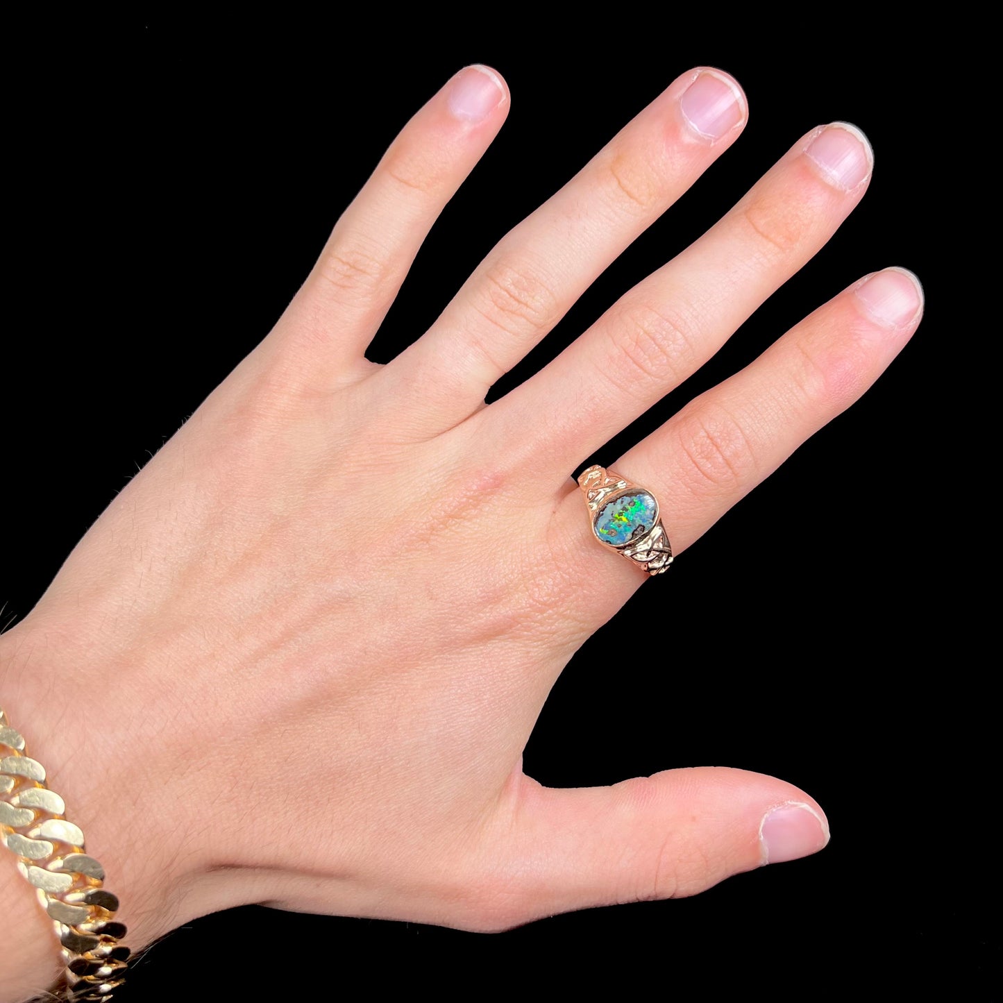 A unisex Celtic style natural boulder opal ring cast in yellow gold. The opal shines green and blue.