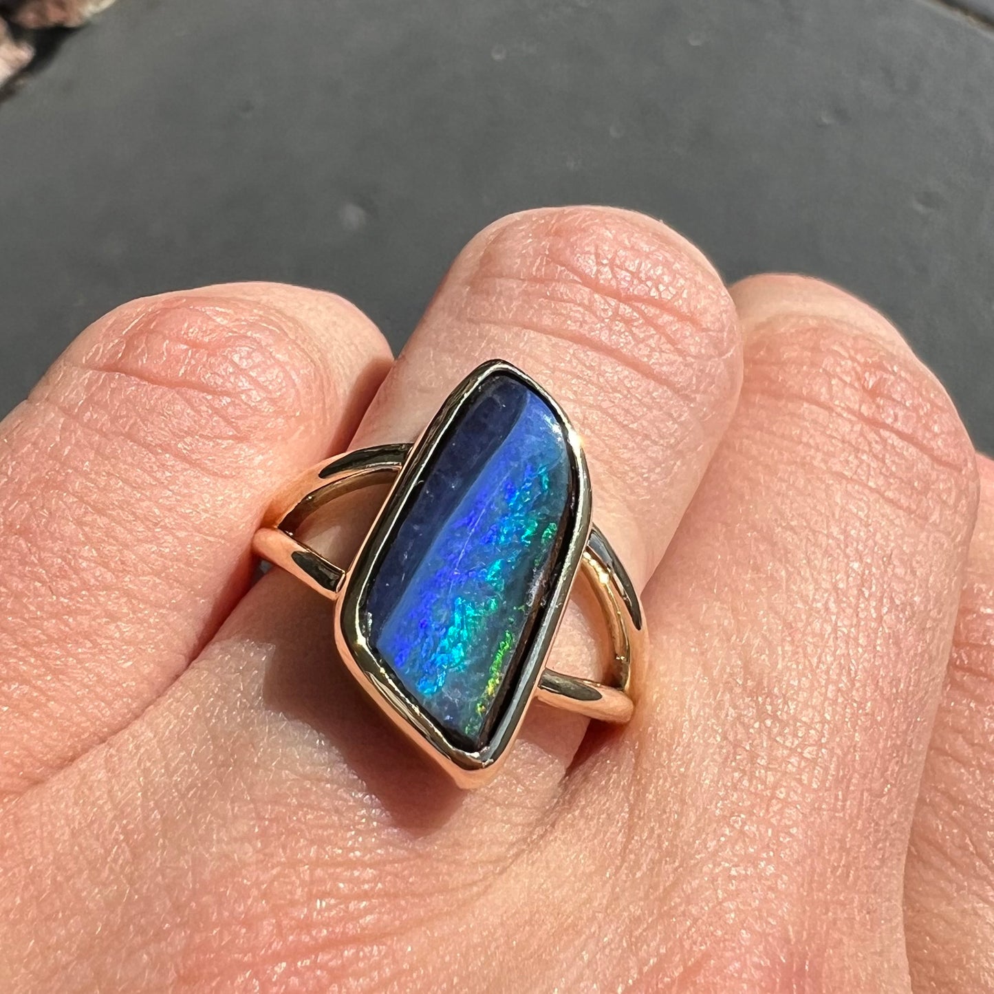 A ladies' split shank gold ring bezel set with a natural, Australian black boulder opal.