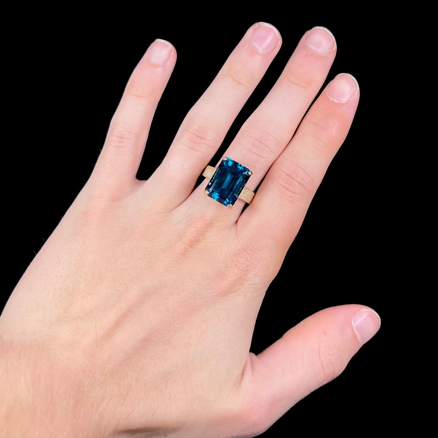 A ladies' yellow gold London blue topaz solitaire ring. The ring is textured, and the topaz is emerald cut.