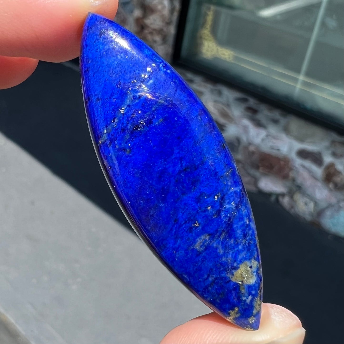 A loose, marquise cabochon cut lapis lazuli stone. The stone has pyrite inclusions.