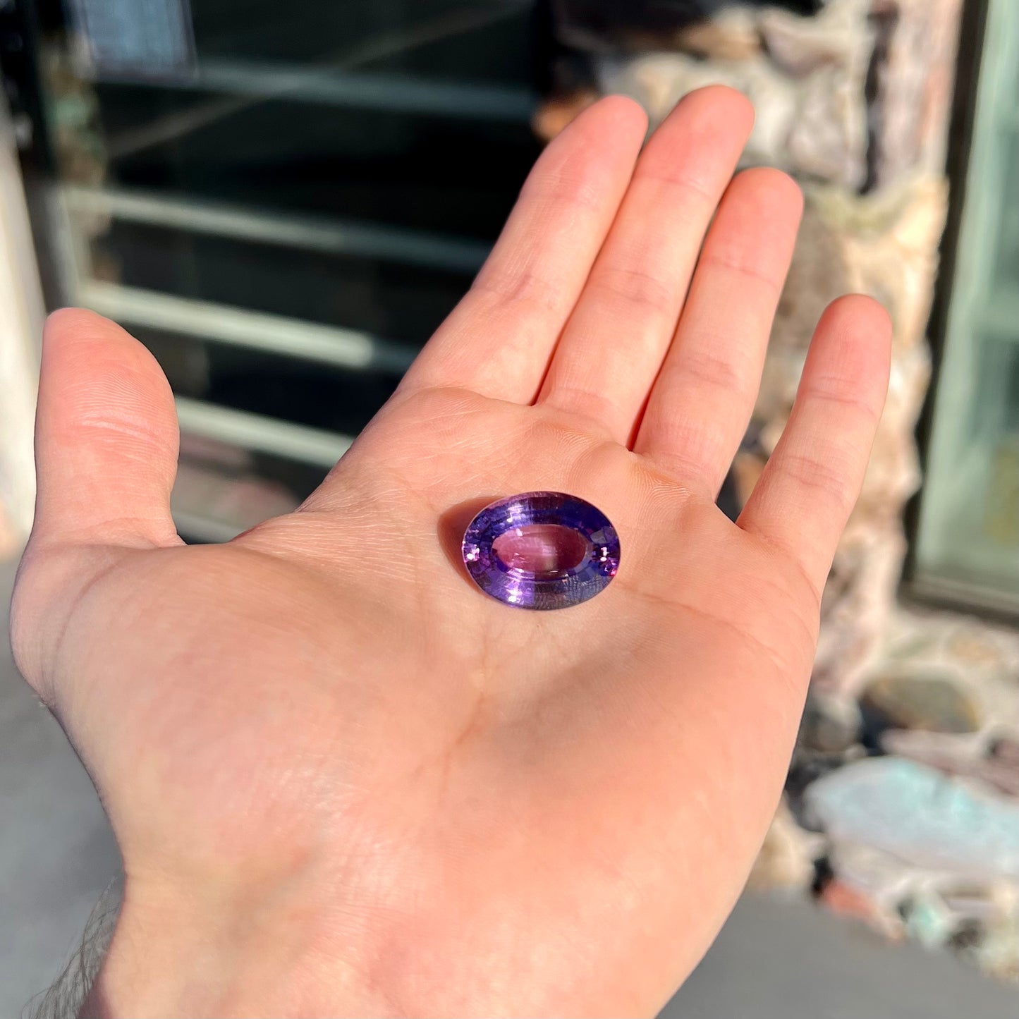 A loose, modified oval step cut amethyst gemstone. There are light scratches to the table.