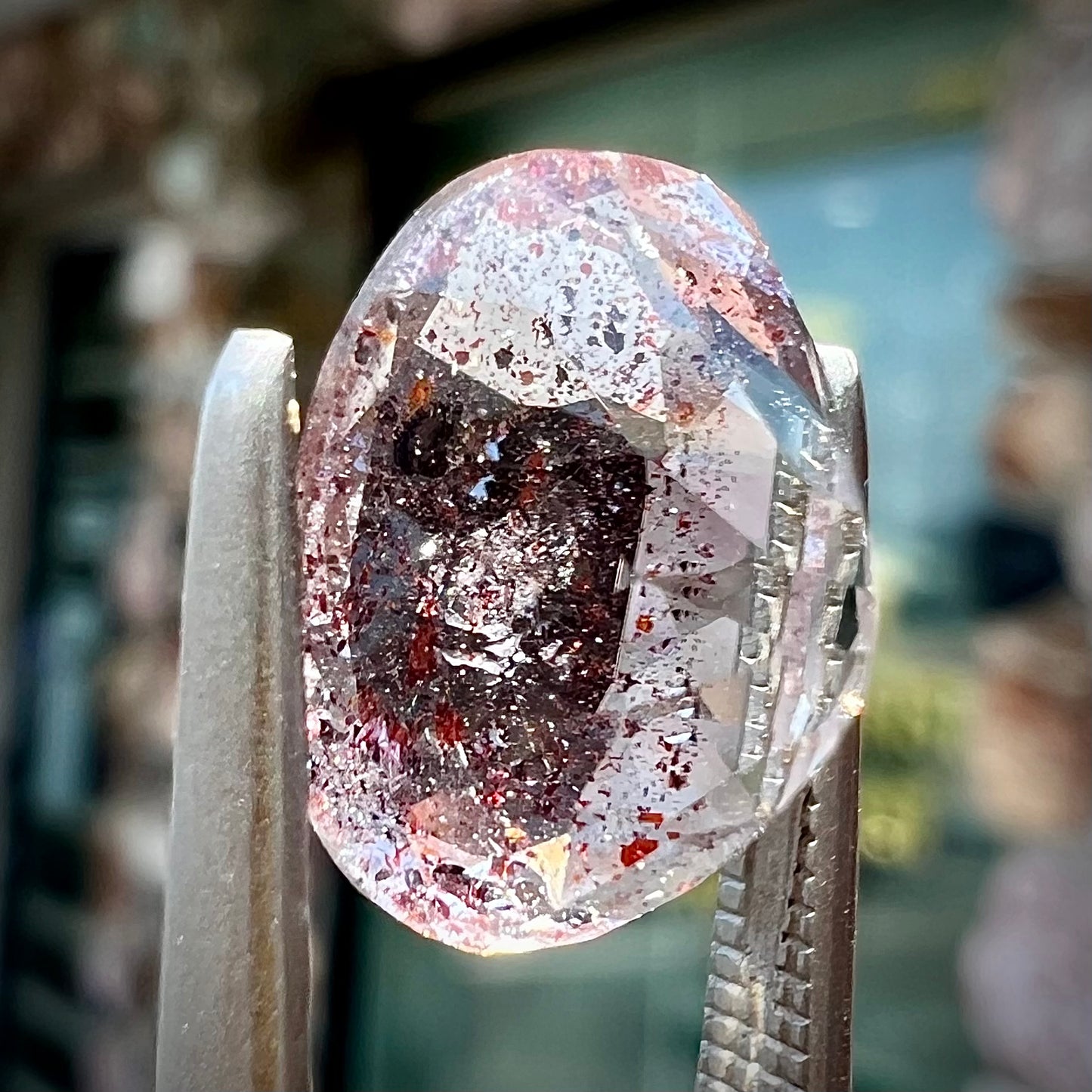 A loose, faceted oval cut lepidocrocite quartz stone. The stone has red and black inclusions.