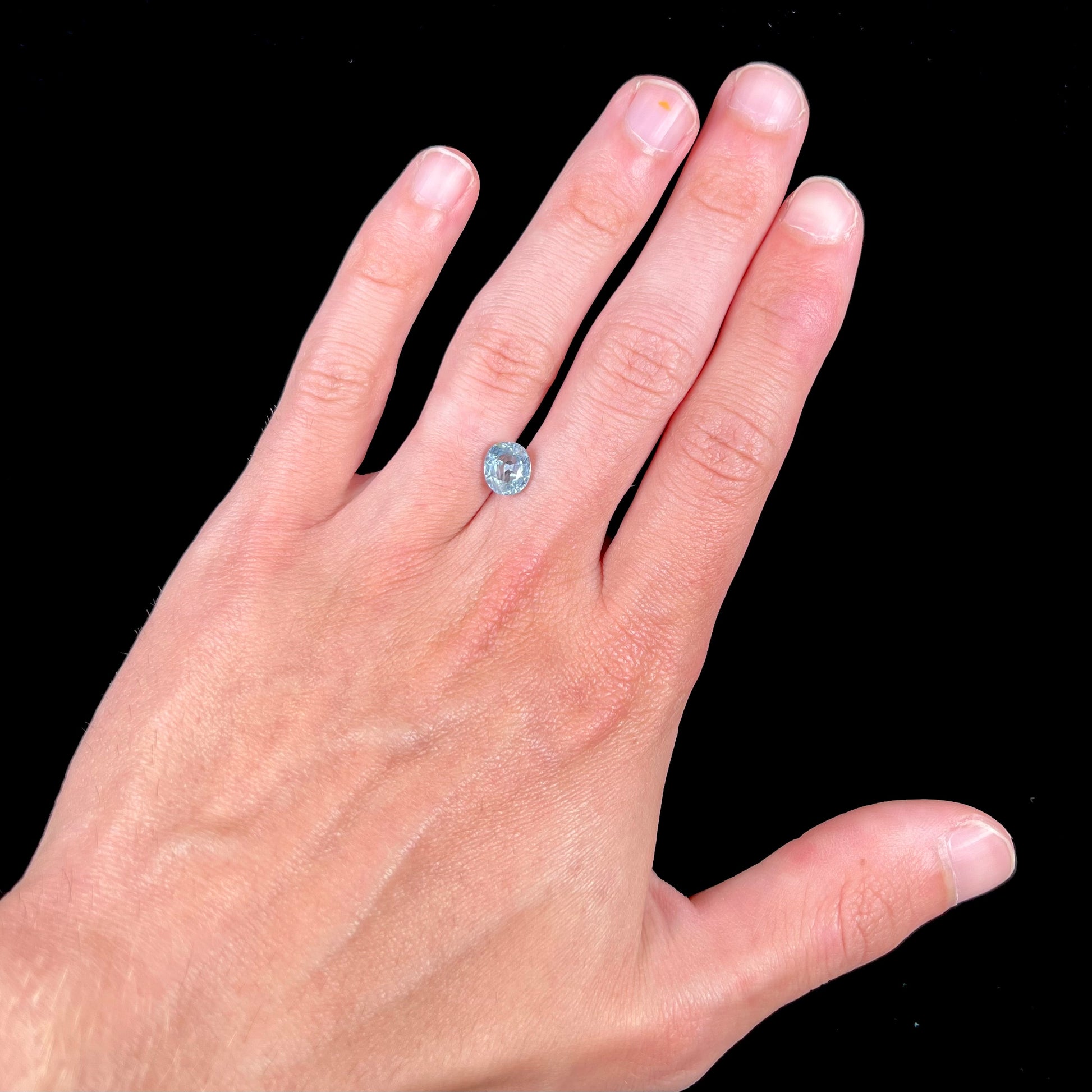 A loose, faceted oval cut light blue natural sapphire gemstone.